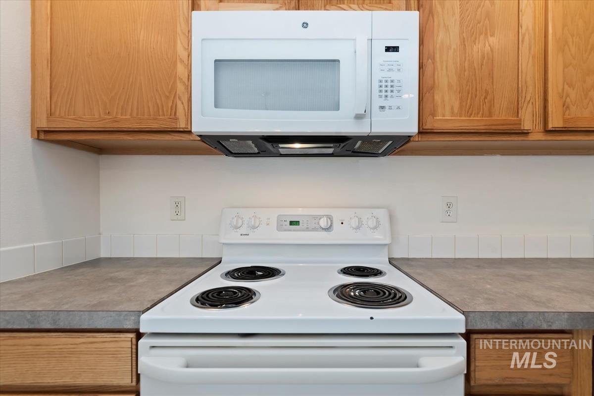 Kitchen featuring white appliances, brown cabinetry, and light countertops