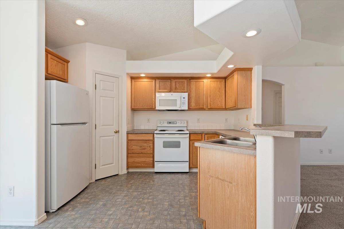 Kitchen with white appliances, a kitchen breakfast bar, a peninsula, light countertops, and recessed lighting