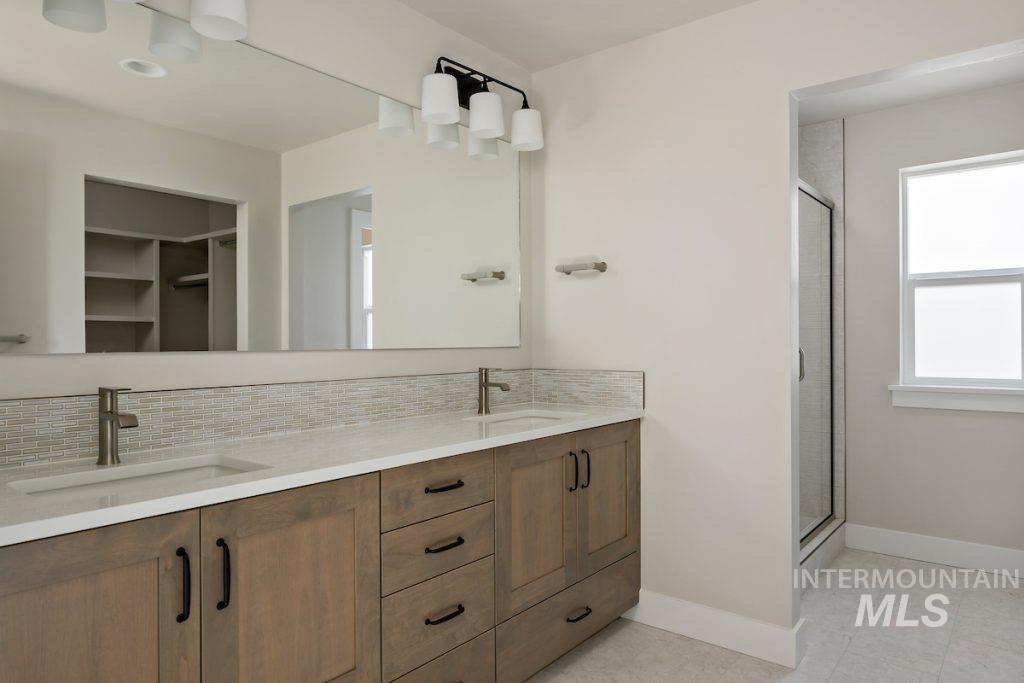 Bathroom featuring double vanity, backsplash, a stall shower, and a walk in closet