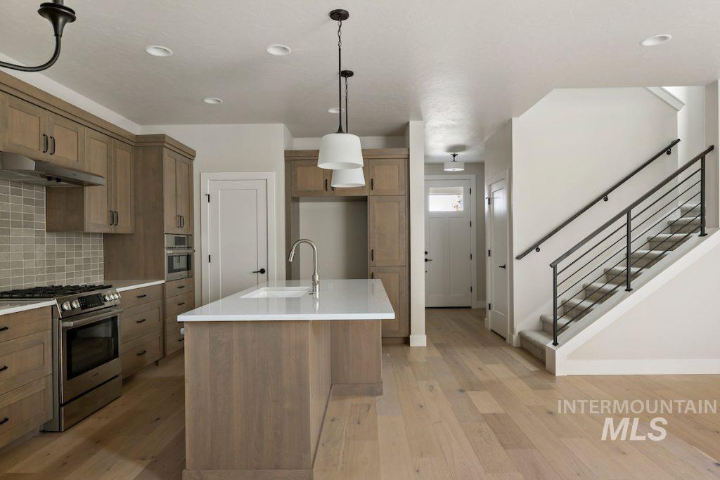 Kitchen featuring appliances with stainless steel finishes, brown cabinets, decorative light fixtures, tasteful backsplash, and an island with sink