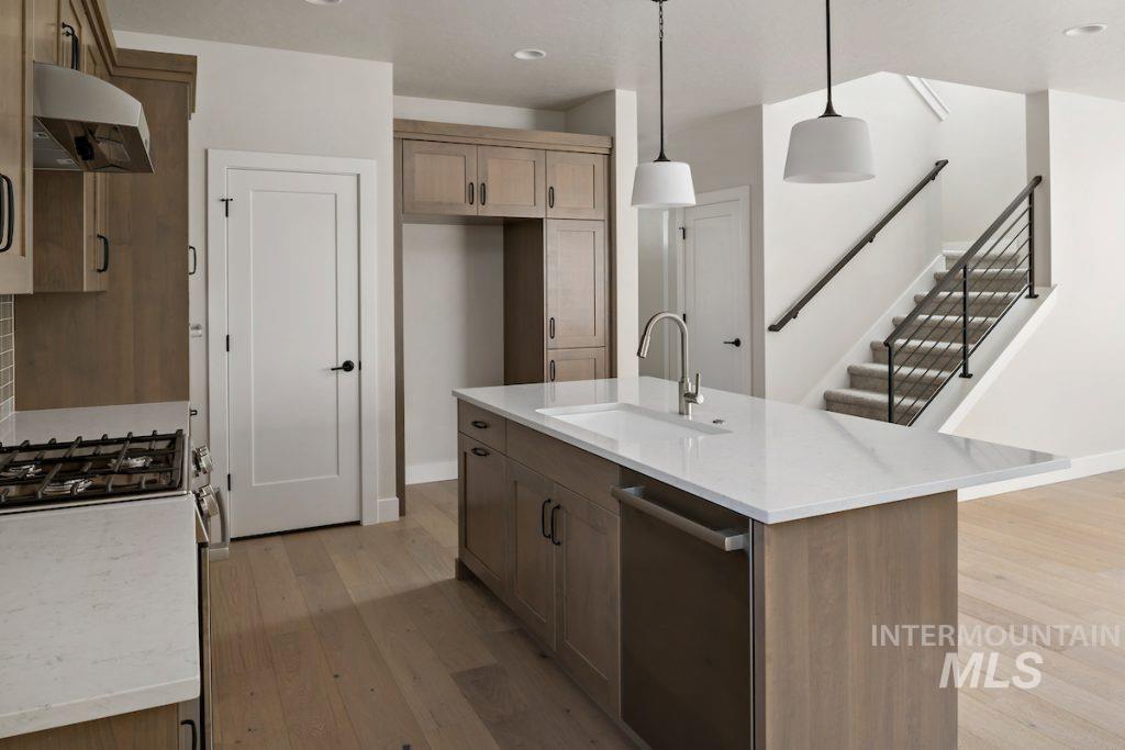 Kitchen featuring pendant lighting, under cabinet range hood, light wood finished floors, stainless steel appliances, and a center island with sink