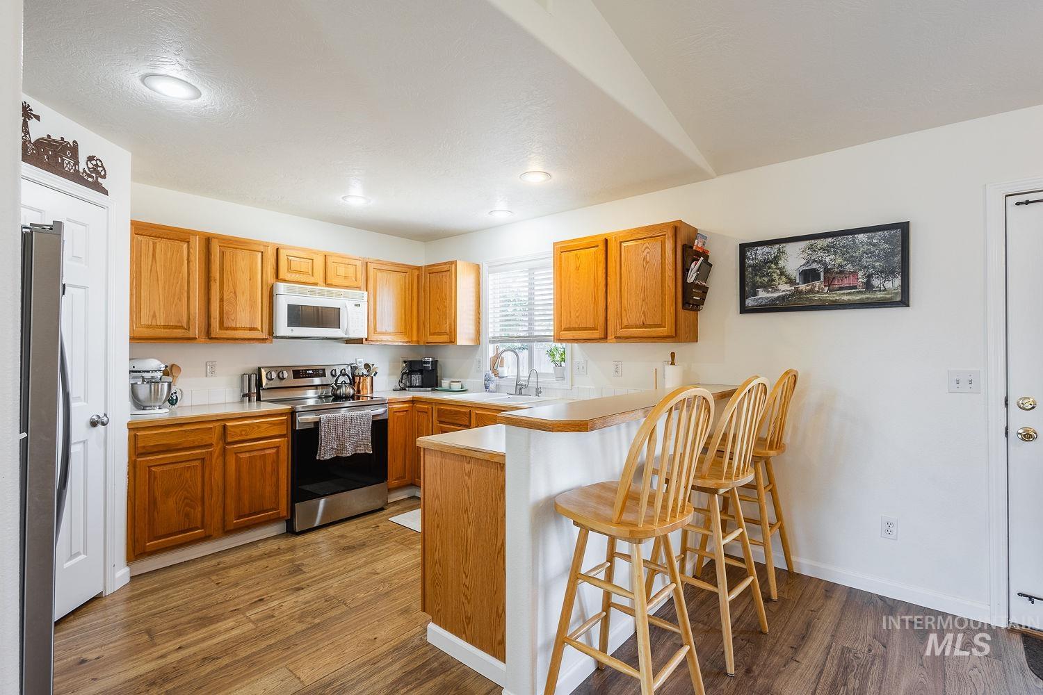 Kitchen with a kitchen bar, stainless steel appliances, light countertops, dark wood-type flooring, and a peninsula