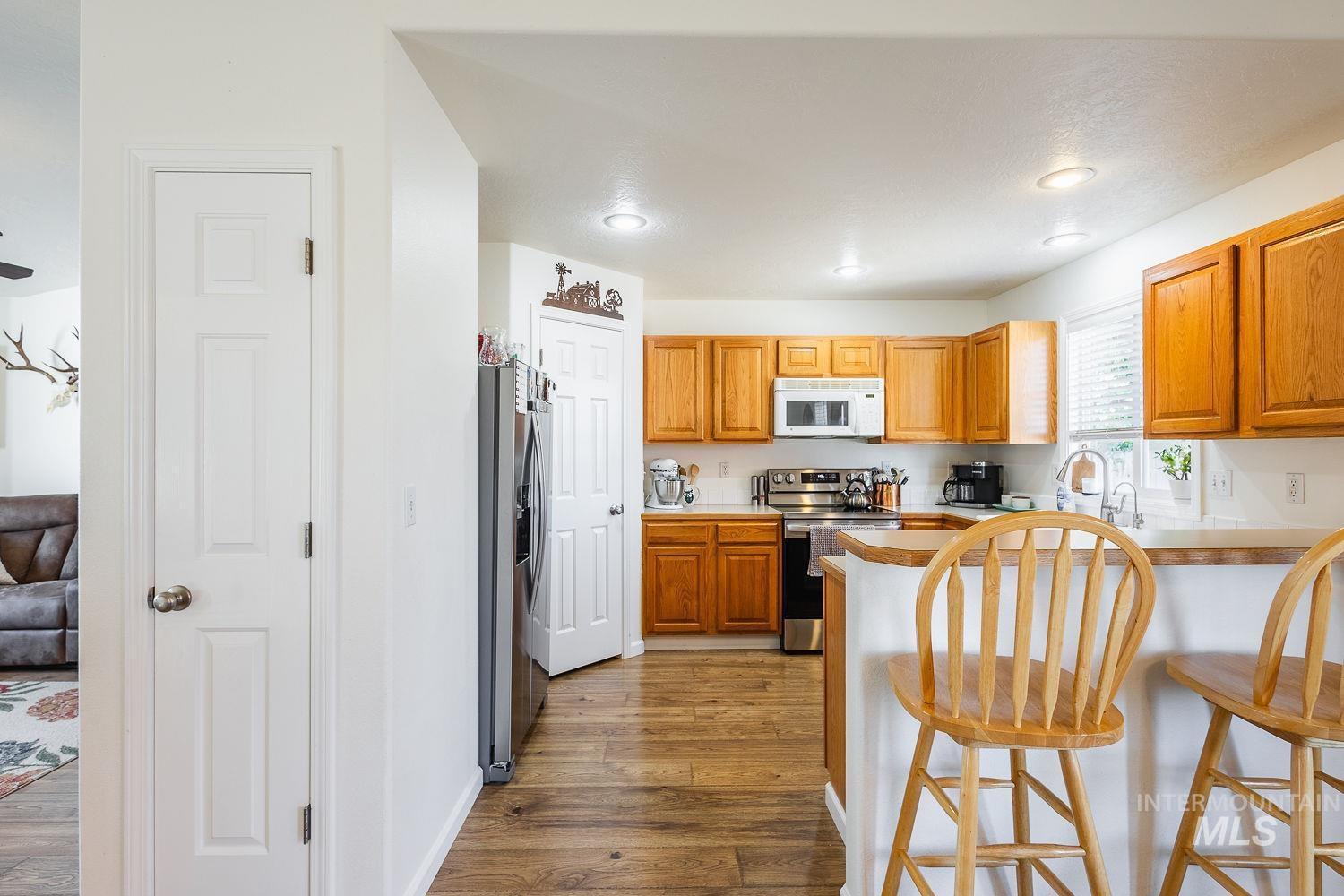 Kitchen featuring appliances with stainless steel finishes, dark wood-style flooring, a breakfast bar, light countertops, and brown cabinetry