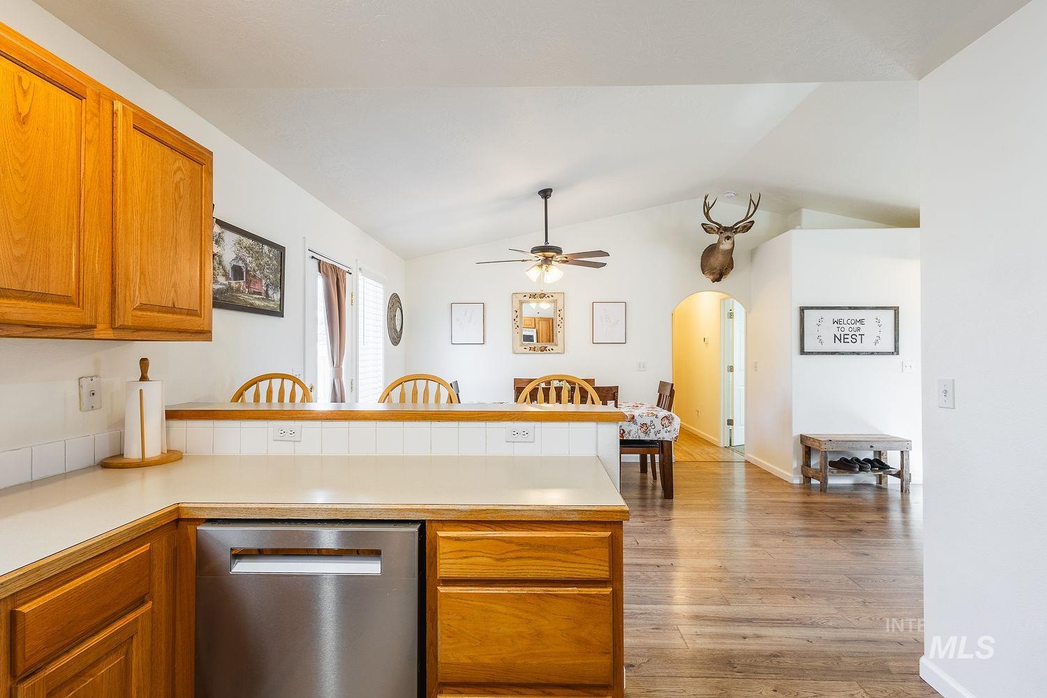 Kitchen featuring light countertops, brown cabinetry, stainless steel dishwasher, lofted ceiling, and light wood-type flooring