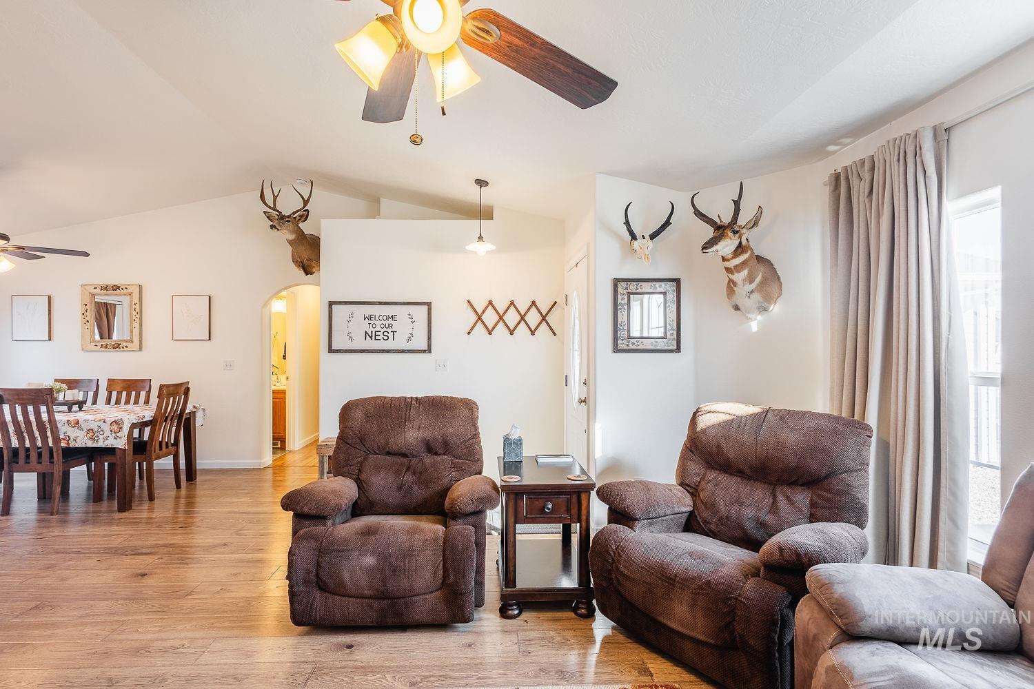 Living room with a ceiling fan, light wood-style floors, lofted ceiling, arched walkways, and plenty of natural light
