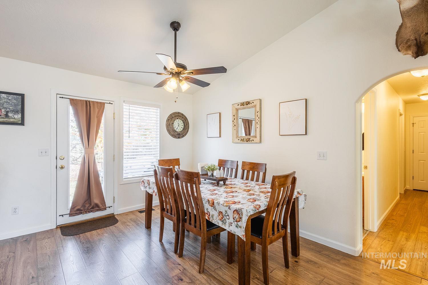Dining space with vaulted ceiling, light wood finished floors, arched walkways, and ceiling fan