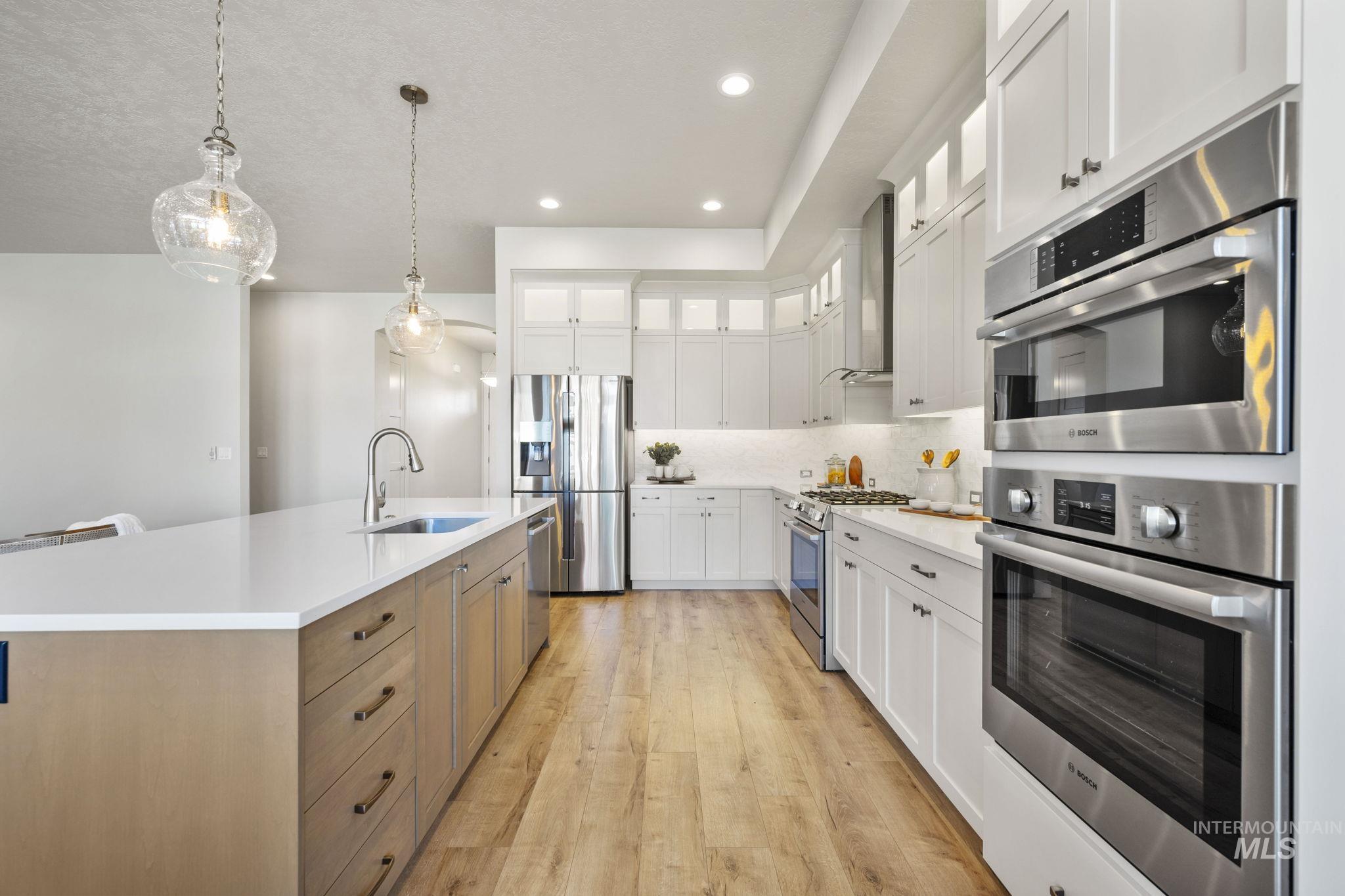 Kitchen with glass insert cabinets, appliances with stainless steel finishes, decorative light fixtures, white cabinetry, and light wood-style flooring