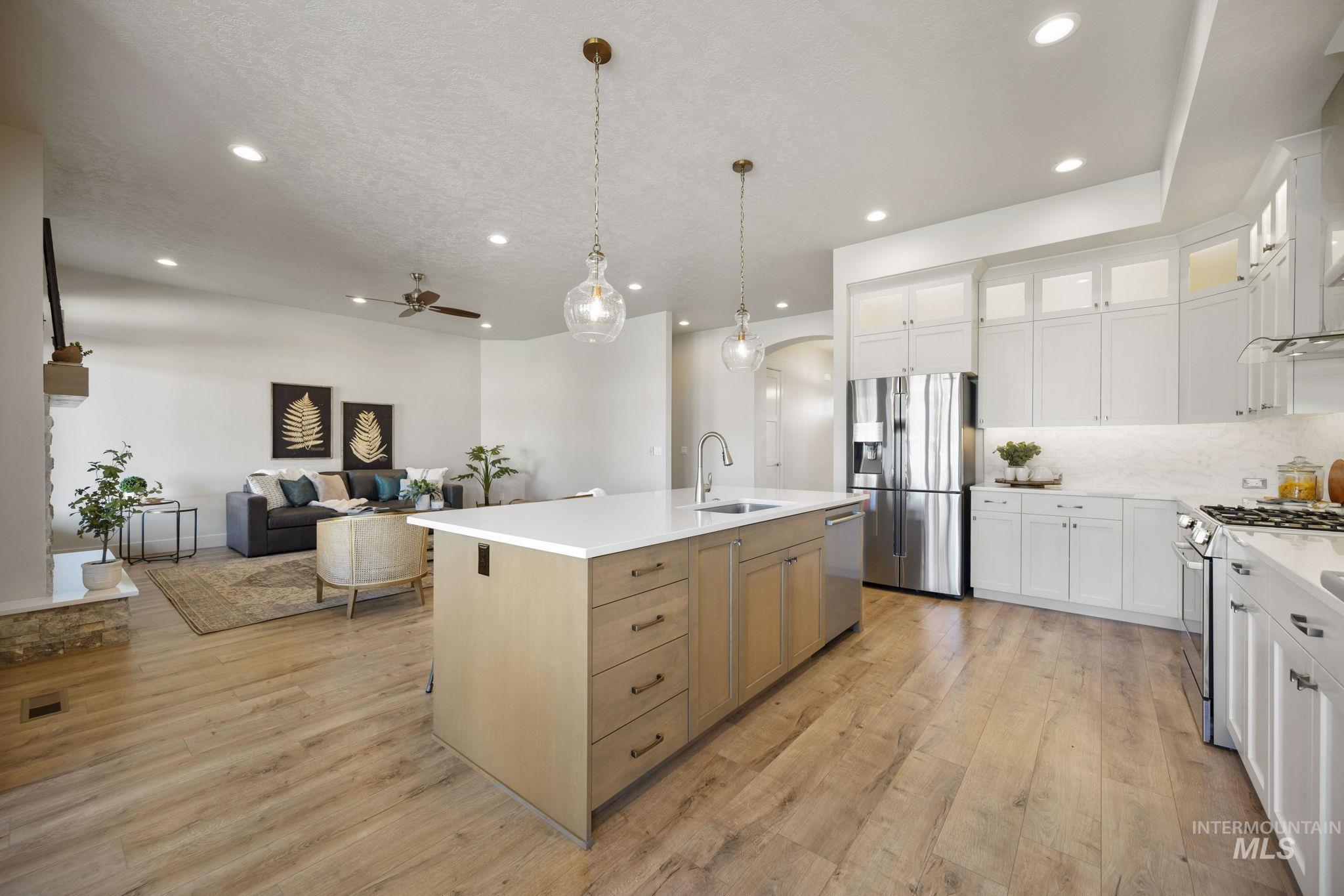 Kitchen with a ceiling fan, stainless steel appliances, white cabinetry, hanging light fixtures, and glass insert cabinets