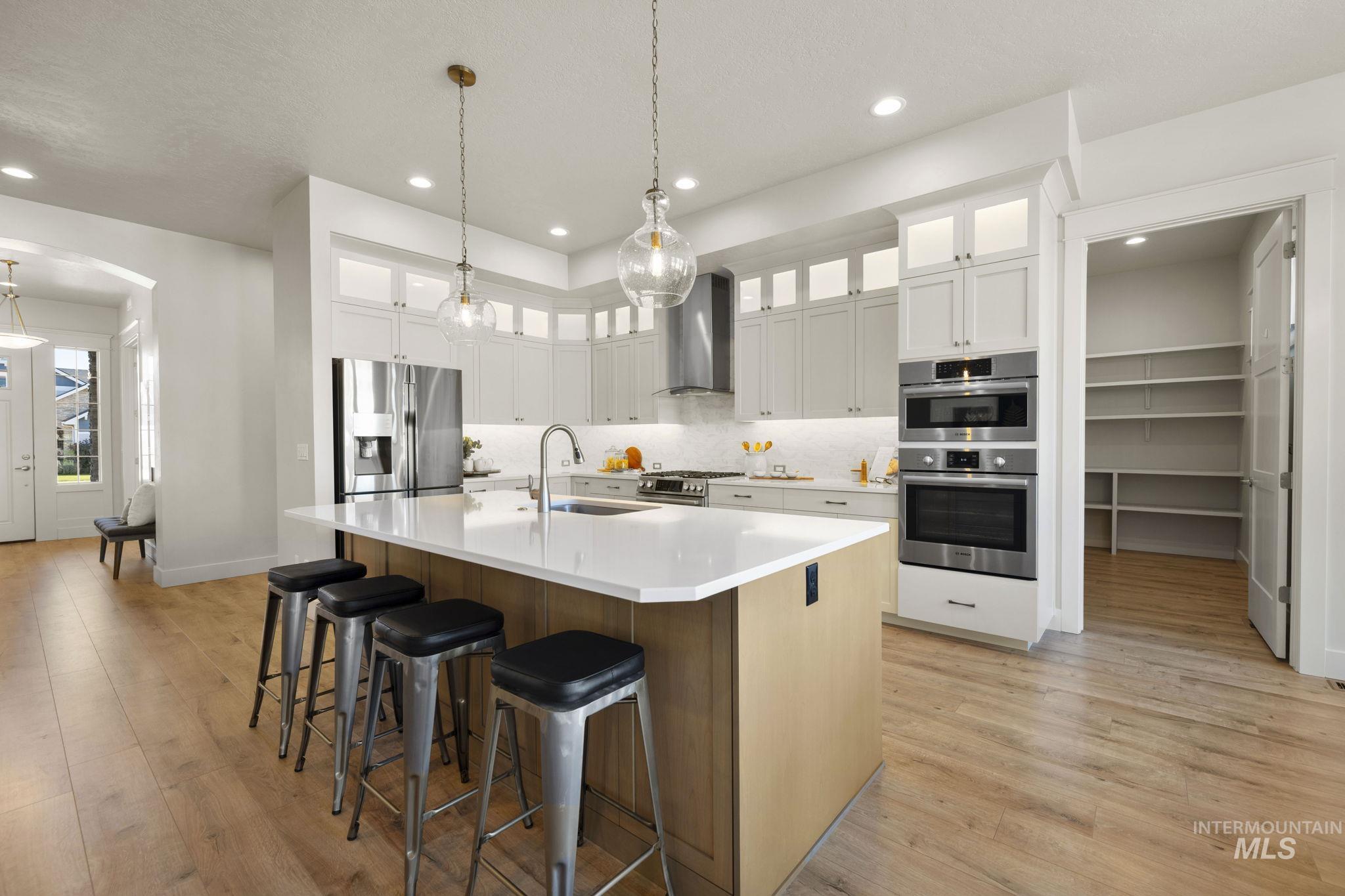 Kitchen featuring white cabinets, a spacious island, stainless steel appliances, glass insert cabinets, and light wood-type flooring