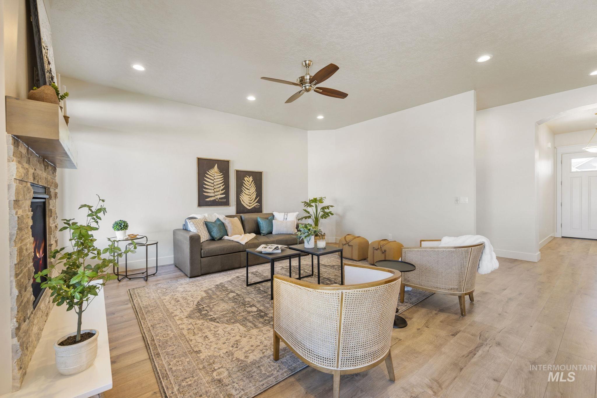 Living area featuring light wood-style flooring, recessed lighting, ceiling fan, a stone fireplace, and a textured ceiling