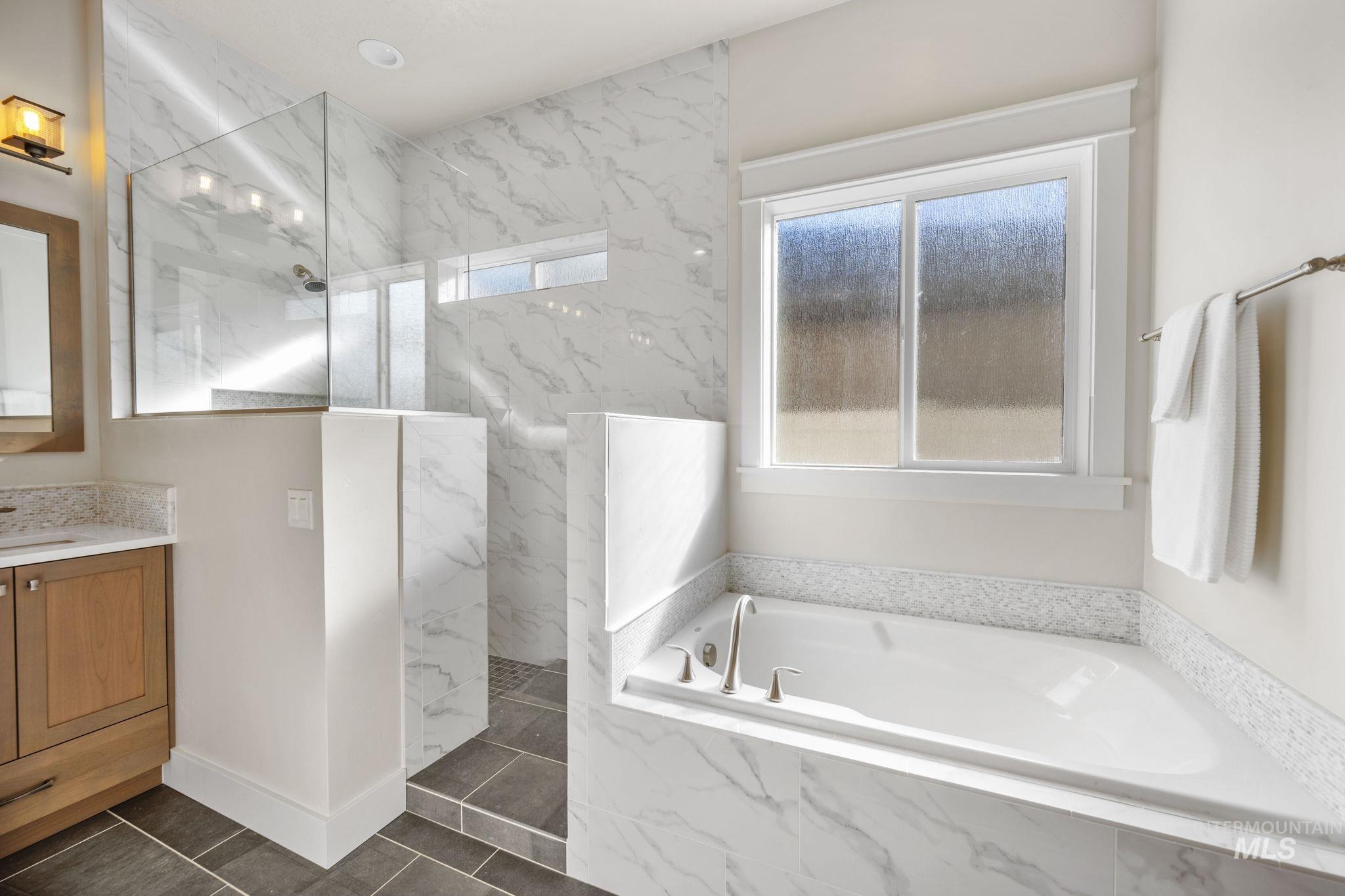 Bathroom with a marble finish shower, a garden tub, vanity, and dark tile patterned flooring