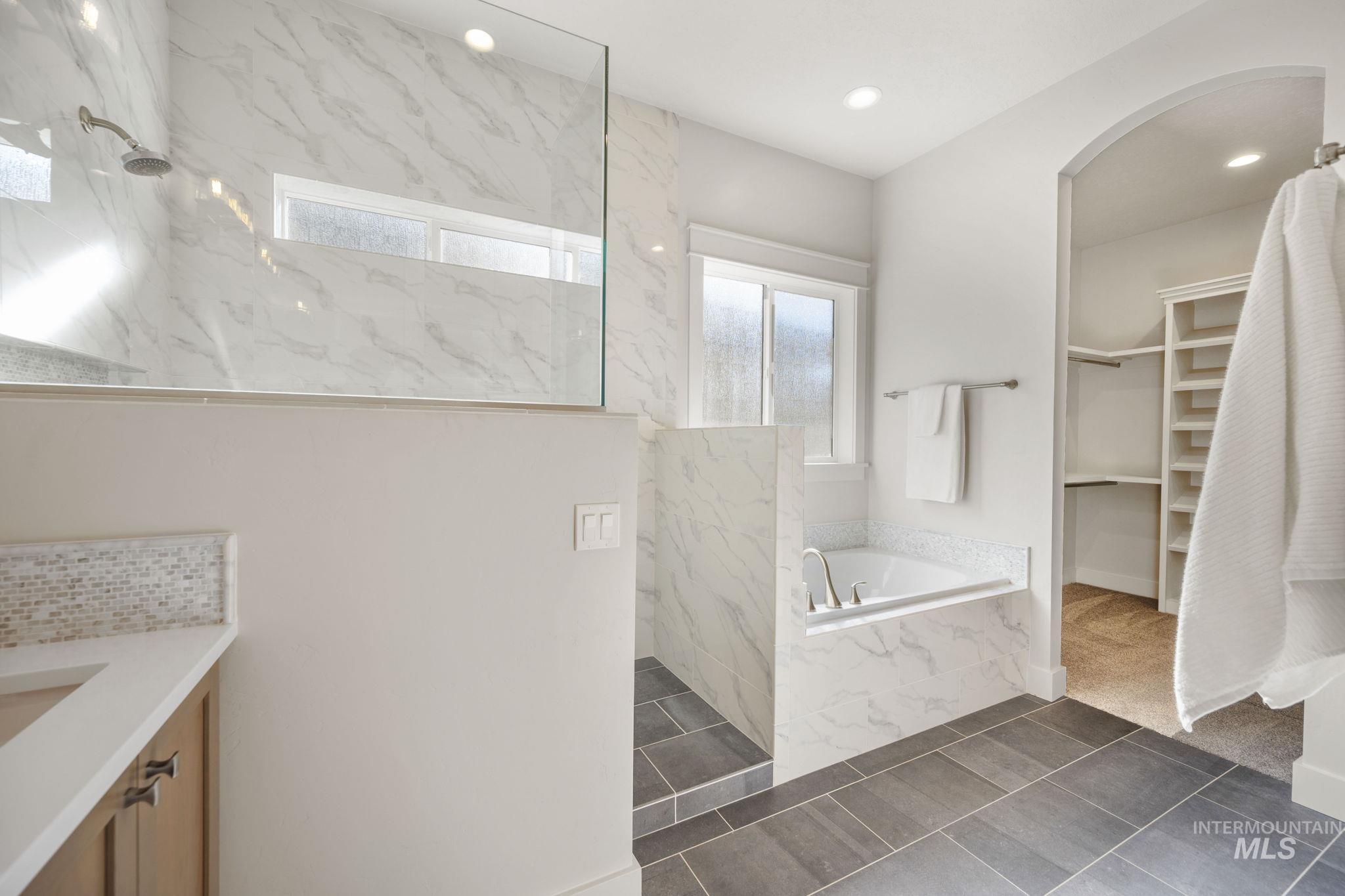 Full bath with a garden tub, a marble finish shower, a walk in closet, dark tile patterned flooring, and recessed lighting