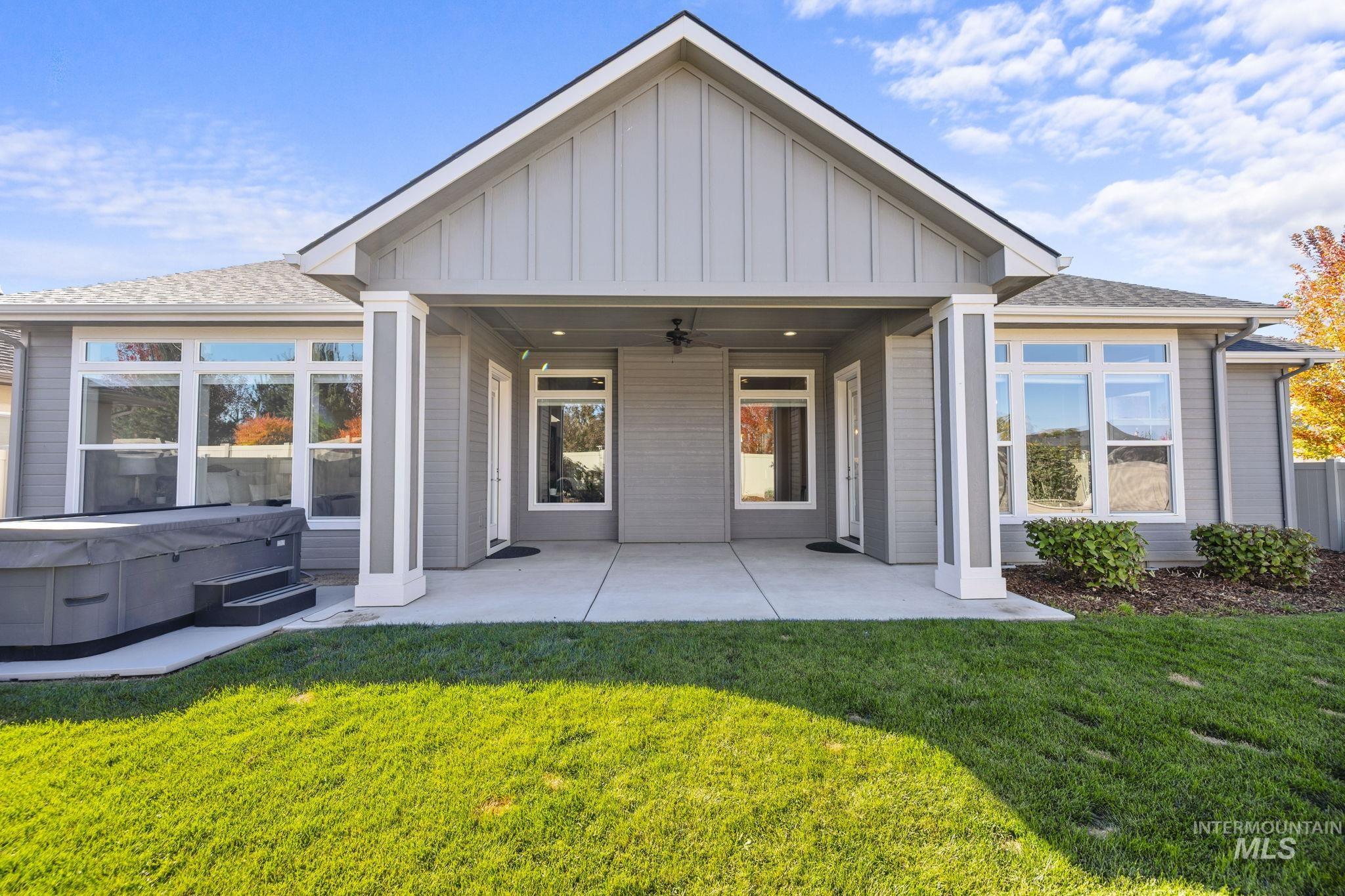 Rear view of house with board and batten siding, a hot tub, a patio, and a lawn