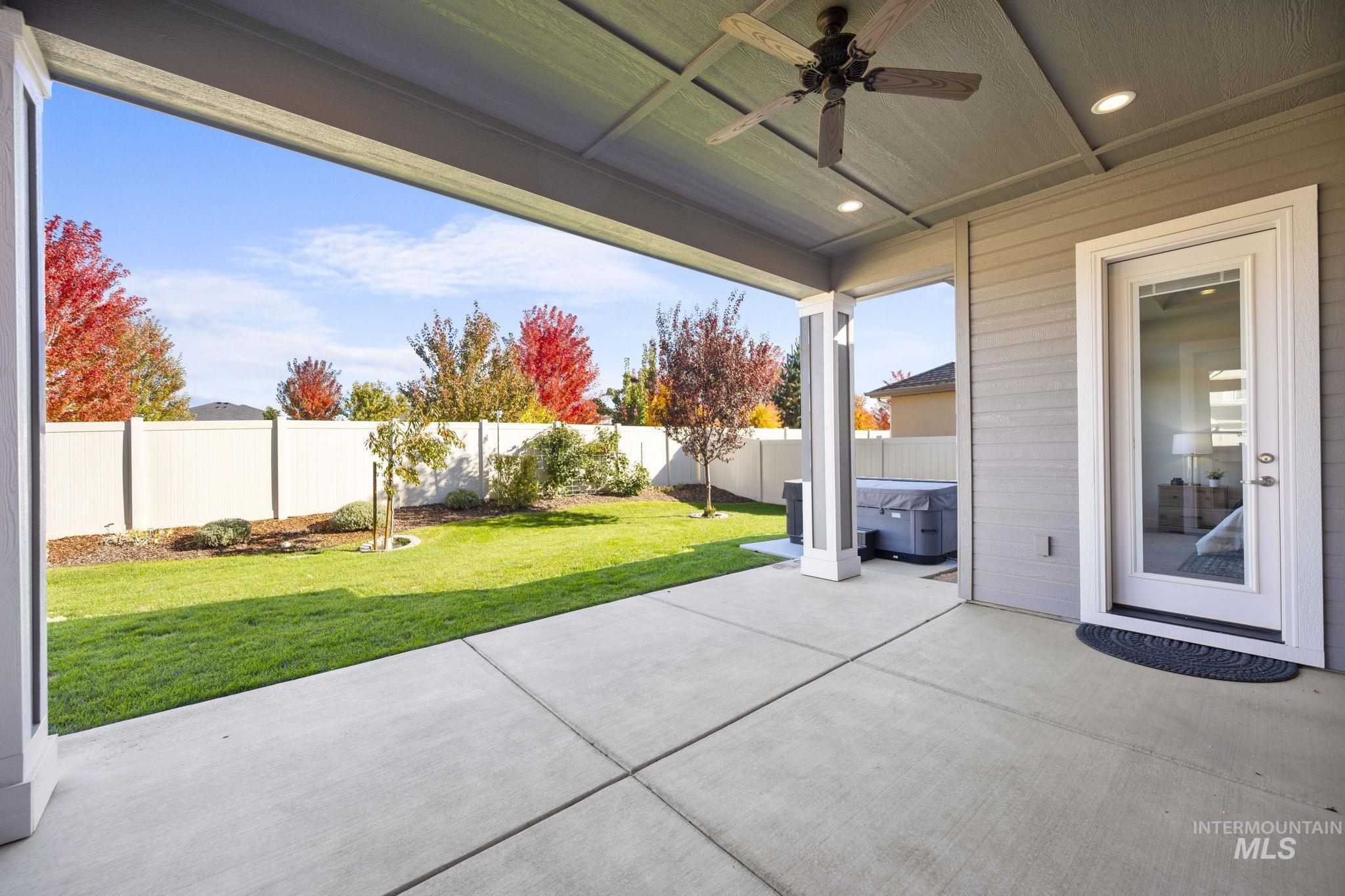 Fenced backyard with ceiling fan, a patio, and a hot tub