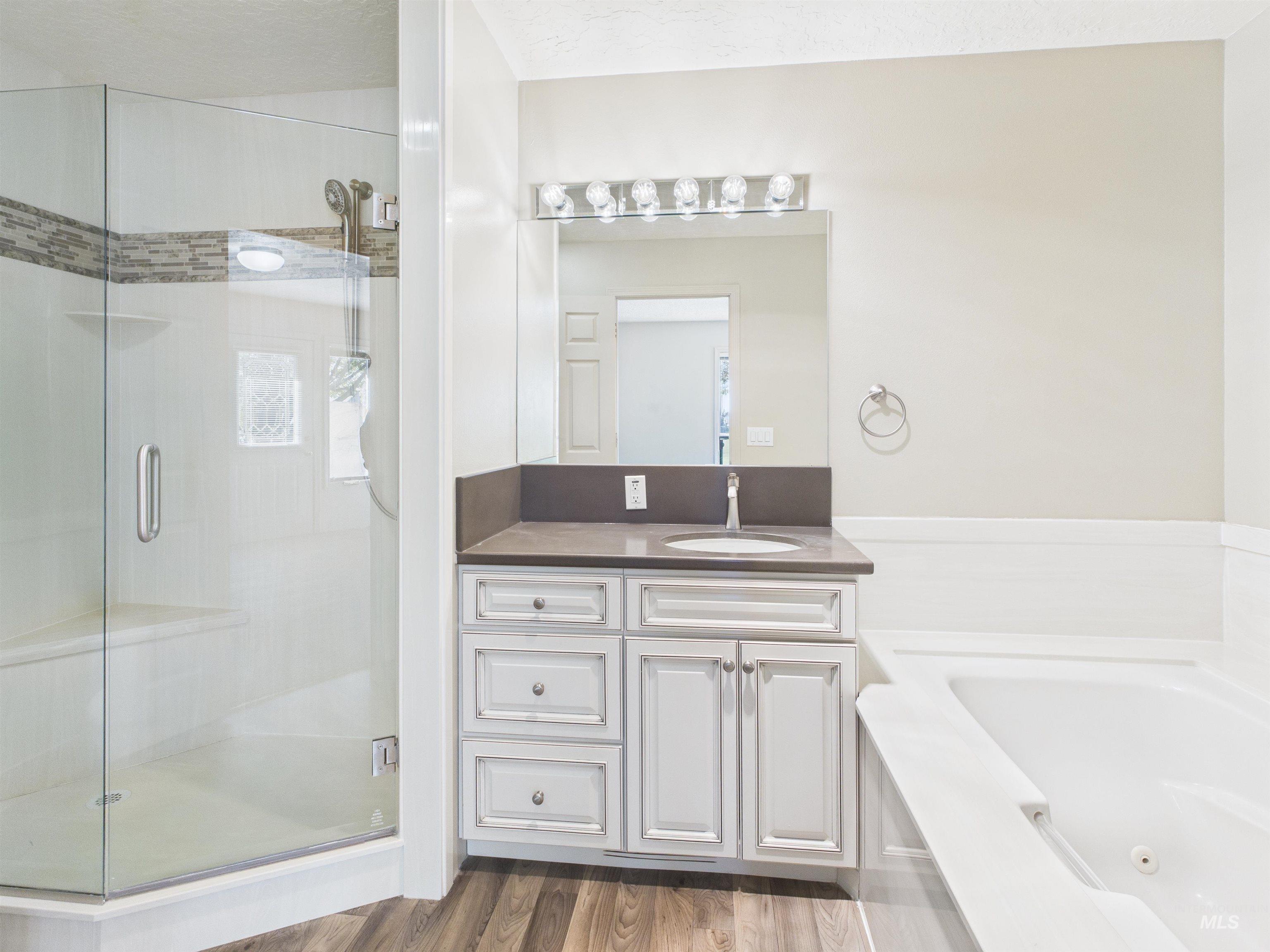 Full bath with vanity, a shower stall, dark wood-type flooring, a tub with jets, and a textured ceiling