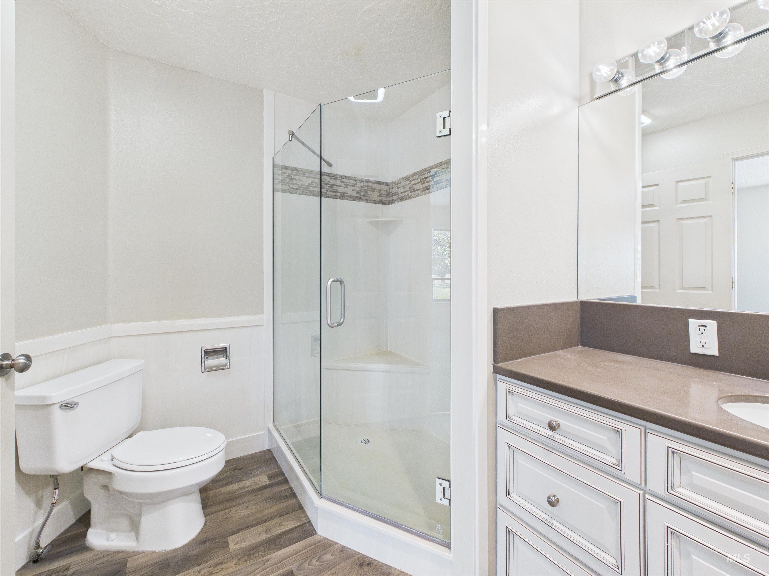 Bathroom with a textured ceiling, a stall shower, dark wood-type flooring, vanity, and a wainscoted wall