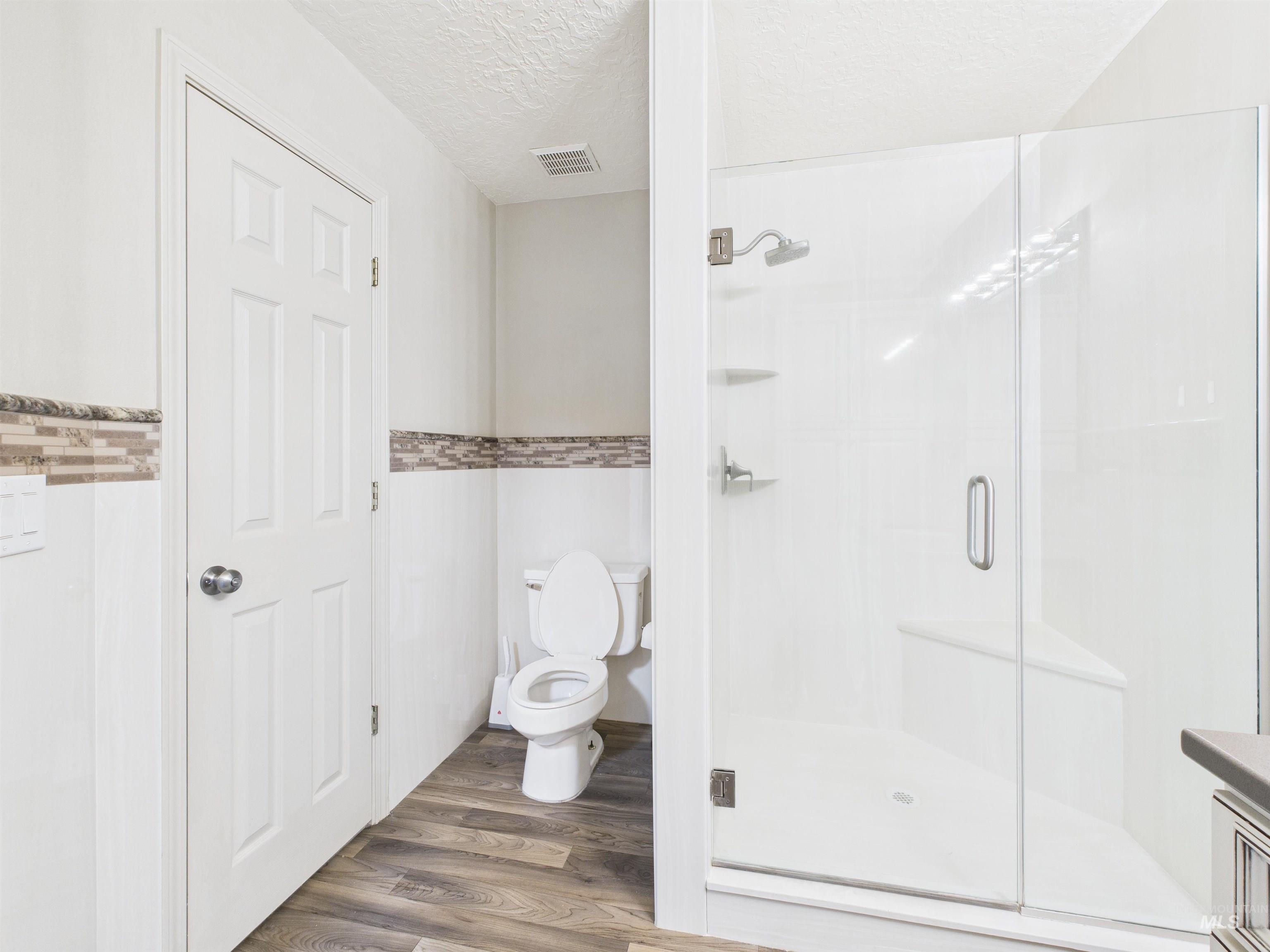 Full bath with dark wood-type flooring, a textured ceiling, a shower stall, and vanity