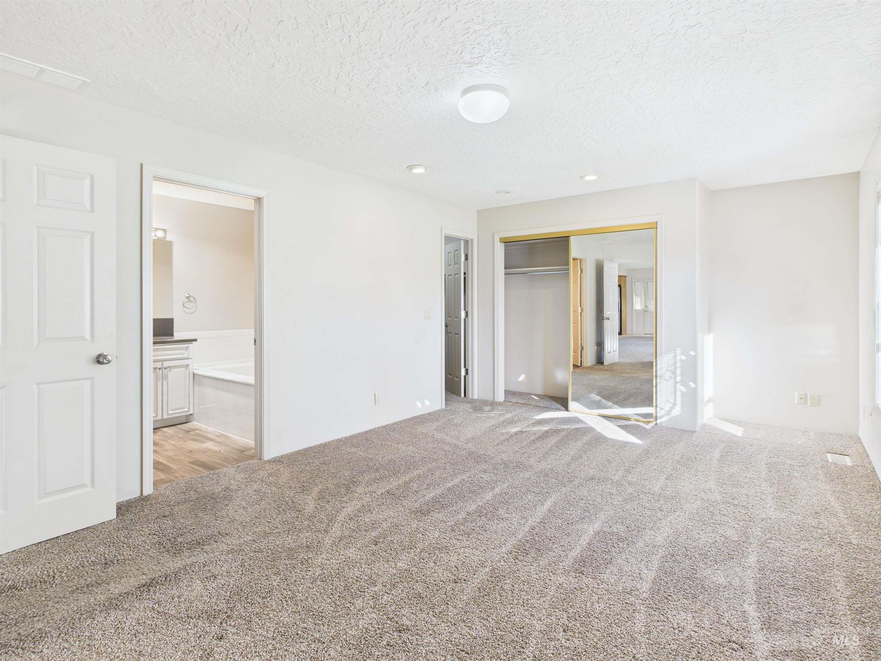 Unfurnished bedroom featuring light colored carpet, a textured ceiling, a closet, and ensuite bath