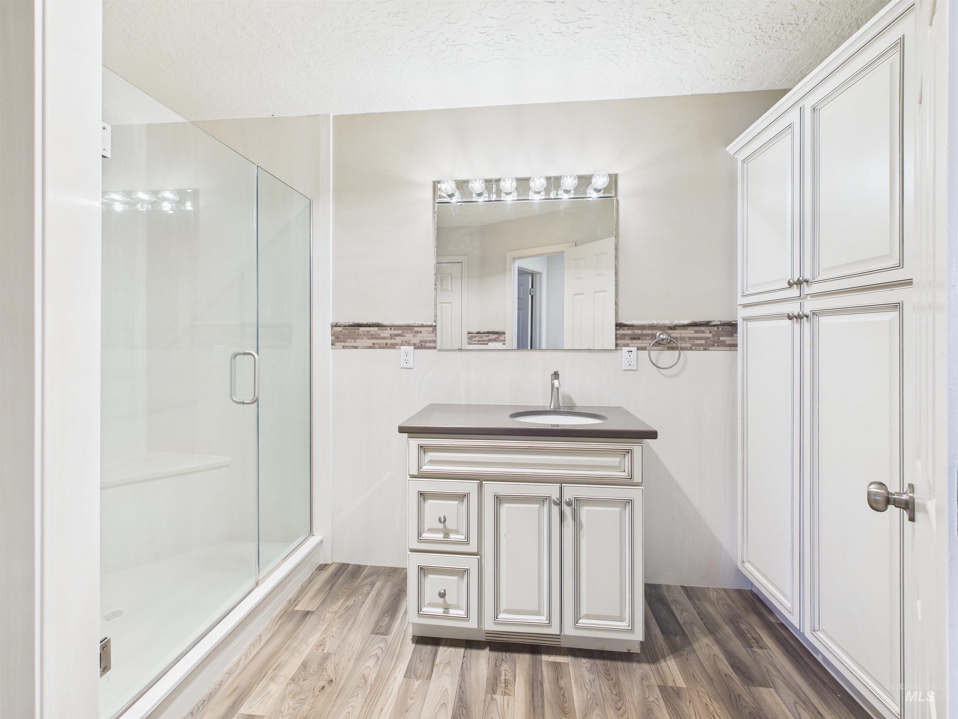 Bathroom with a shower stall, a textured ceiling, vanity, and light wood-type flooring