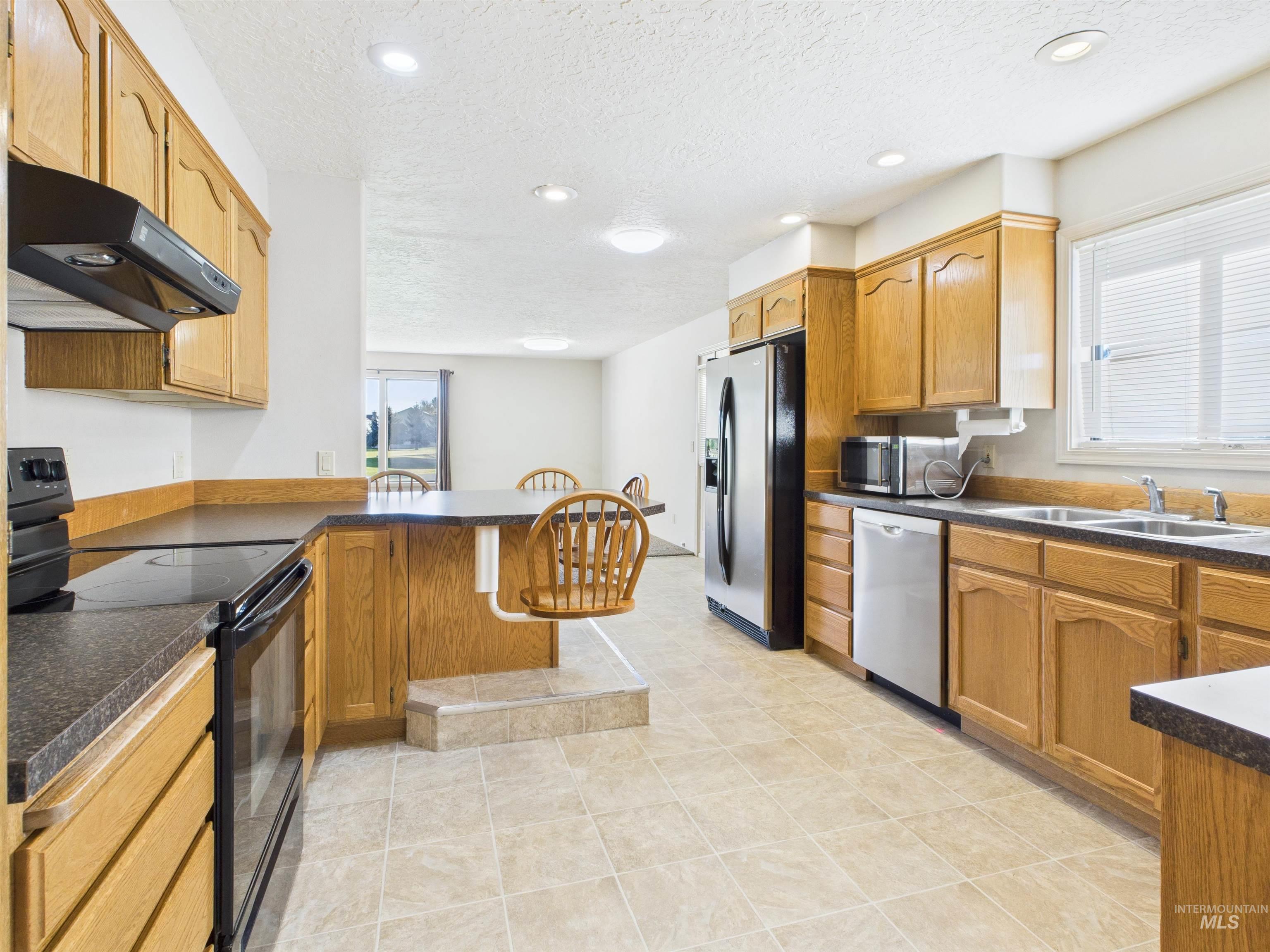 Kitchen with dark countertops, stainless steel appliances, a peninsula, a kitchen bar, and a textured ceiling