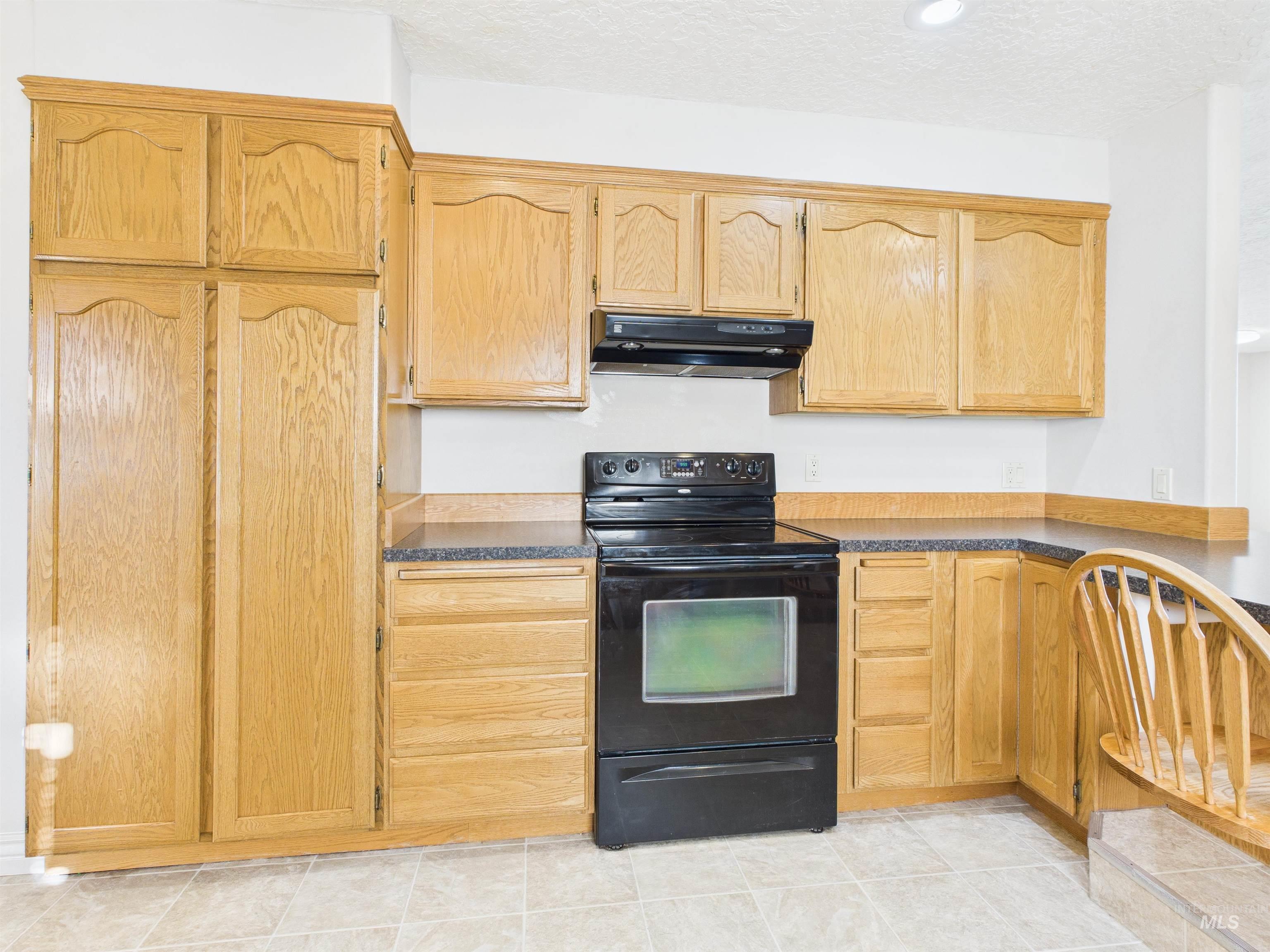 Kitchen featuring black electric range, dark countertops, a textured ceiling, under cabinet range hood, and light tile patterned floors