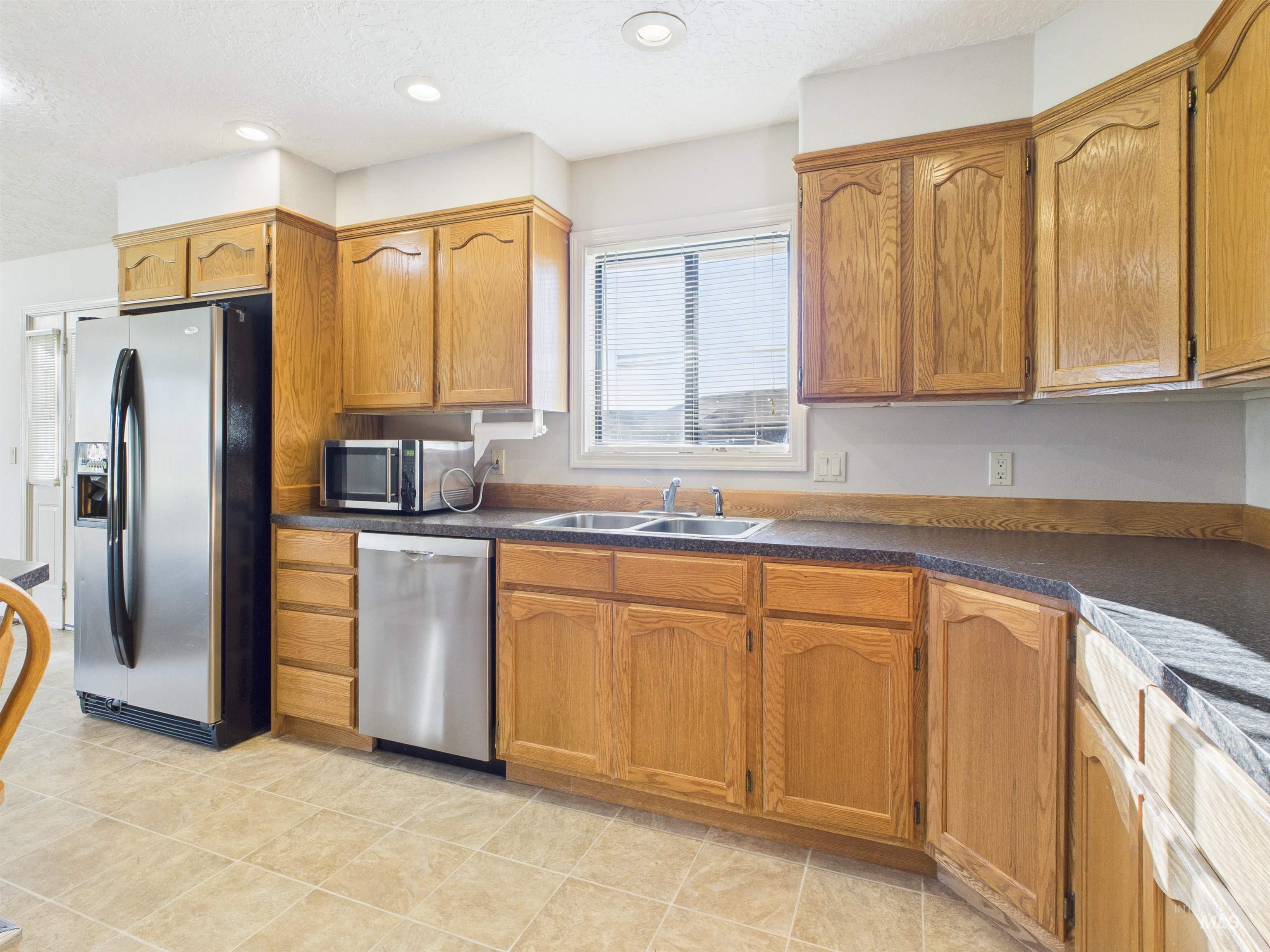 Kitchen featuring a textured ceiling, appliances with stainless steel finishes, brown cabinetry, dark countertops, and recessed lighting