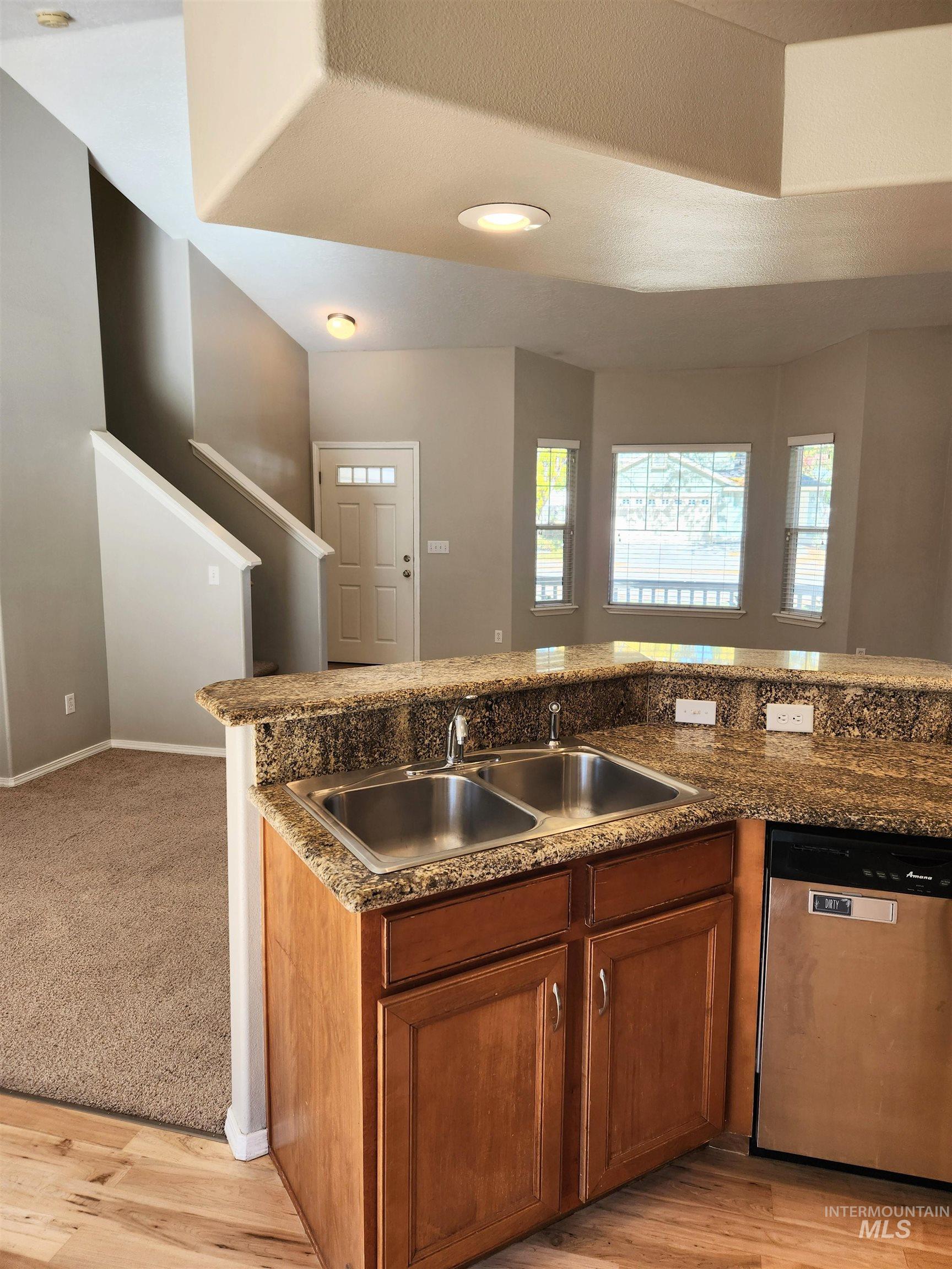 Kitchen featuring brown cabinetry, stainless steel dishwasher, light wood-style flooring, and open floor plan