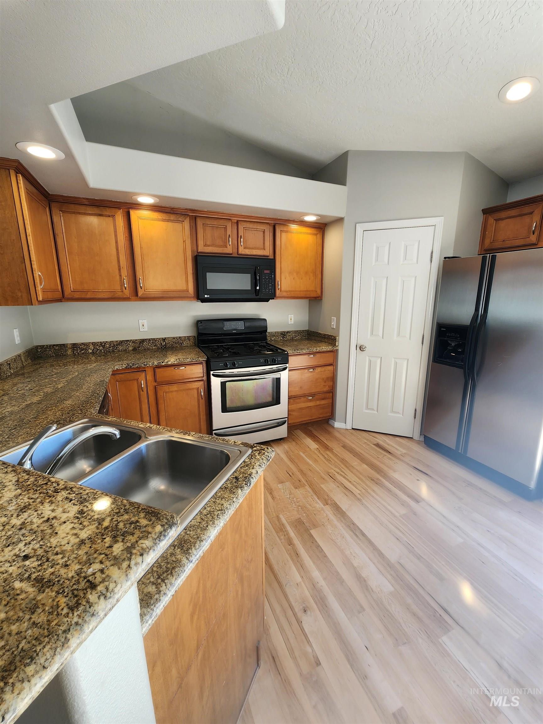Kitchen featuring recessed lighting, appliances with stainless steel finishes, brown cabinets, dark stone counters, and light wood finished floors