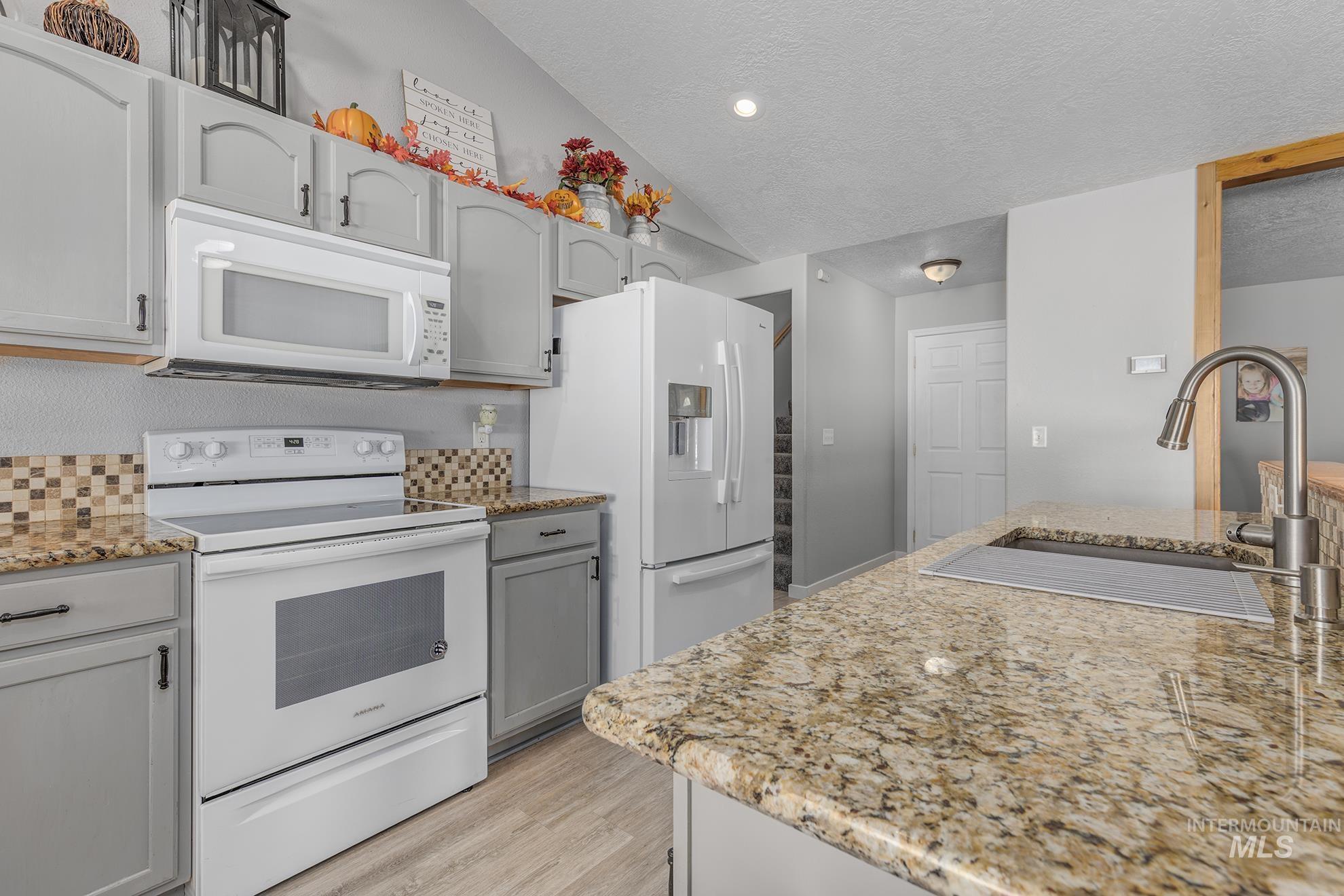 Kitchen with white appliances, a textured ceiling, light stone countertops, light wood-type flooring, and gray cabinetry