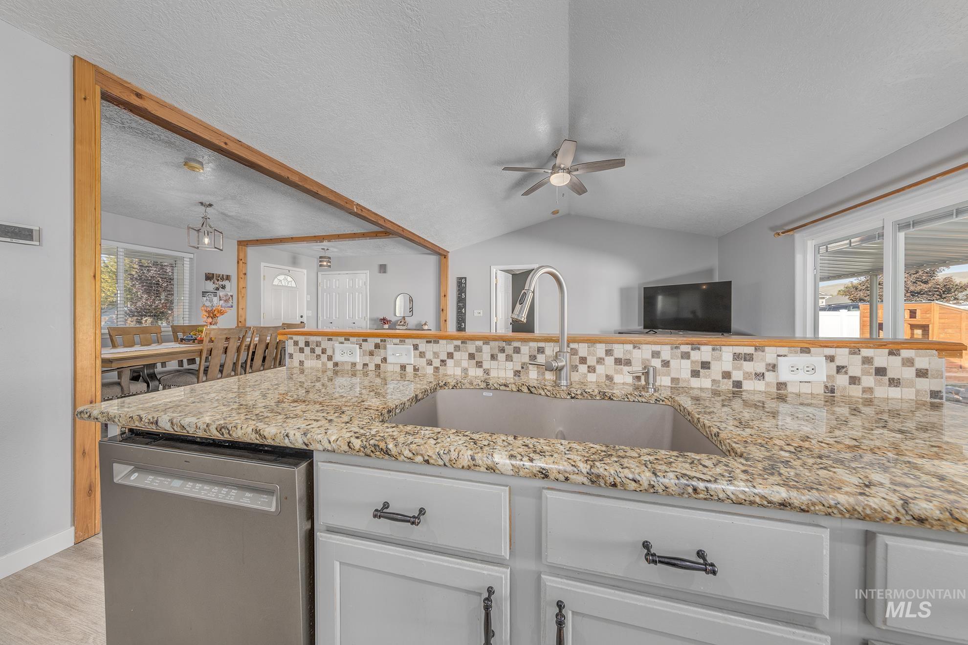 Kitchen featuring stainless steel dishwasher, light stone counters, a textured ceiling, lofted ceiling, and white cabinetry