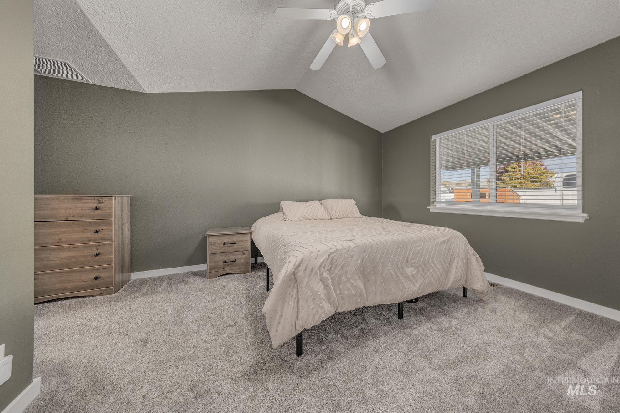 Carpeted bedroom with lofted ceiling, a textured ceiling, and a ceiling fan