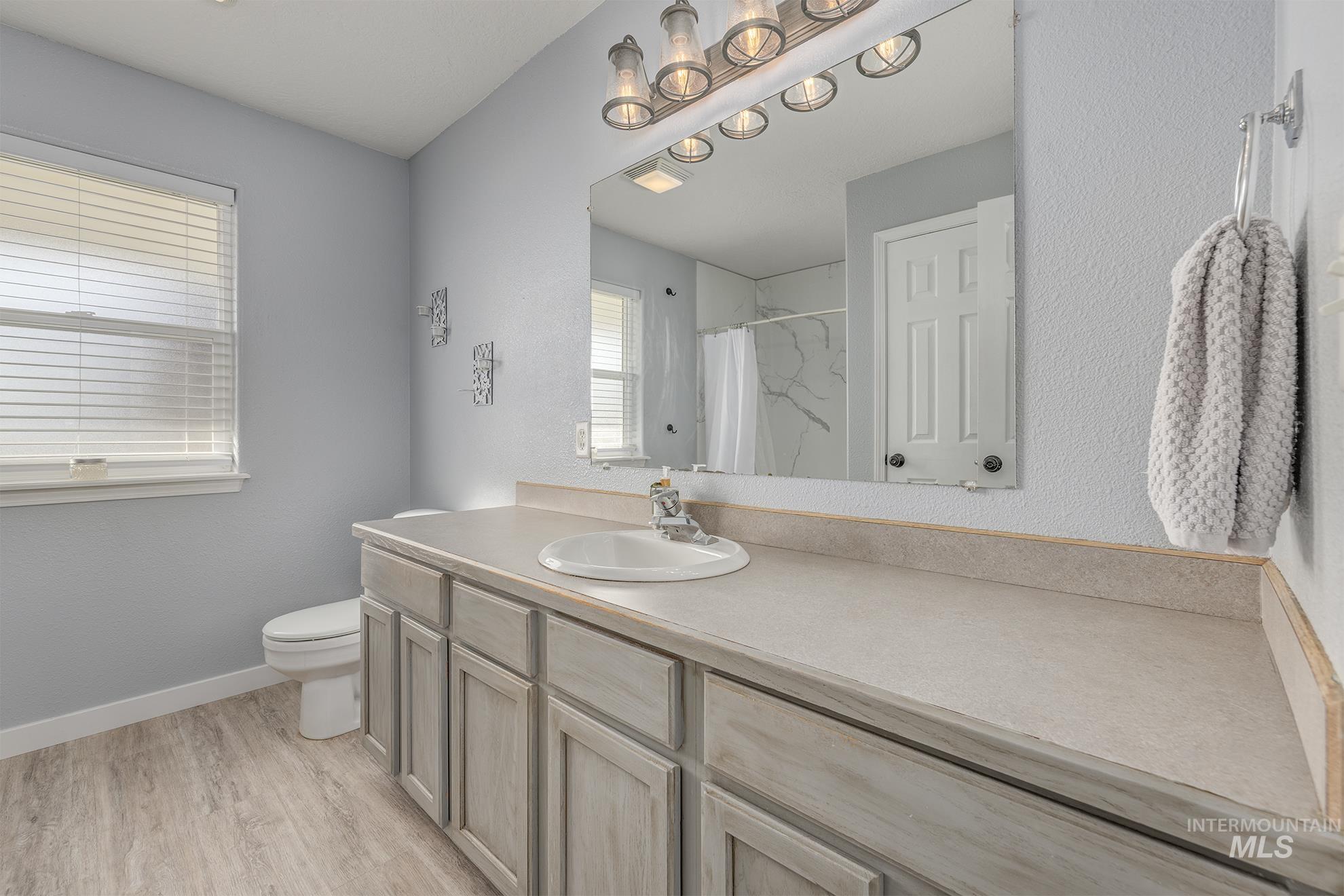 Full bath featuring a marble finish shower, vanity, light wood-style floors, and a textured wall