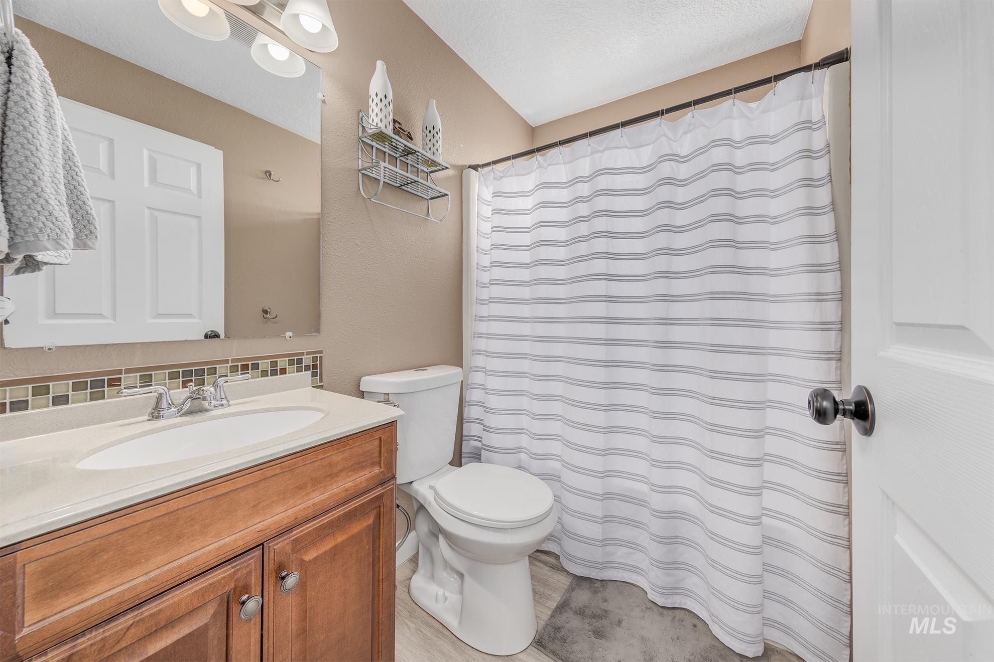 Full bath with a shower with shower curtain, vanity, and tasteful backsplash