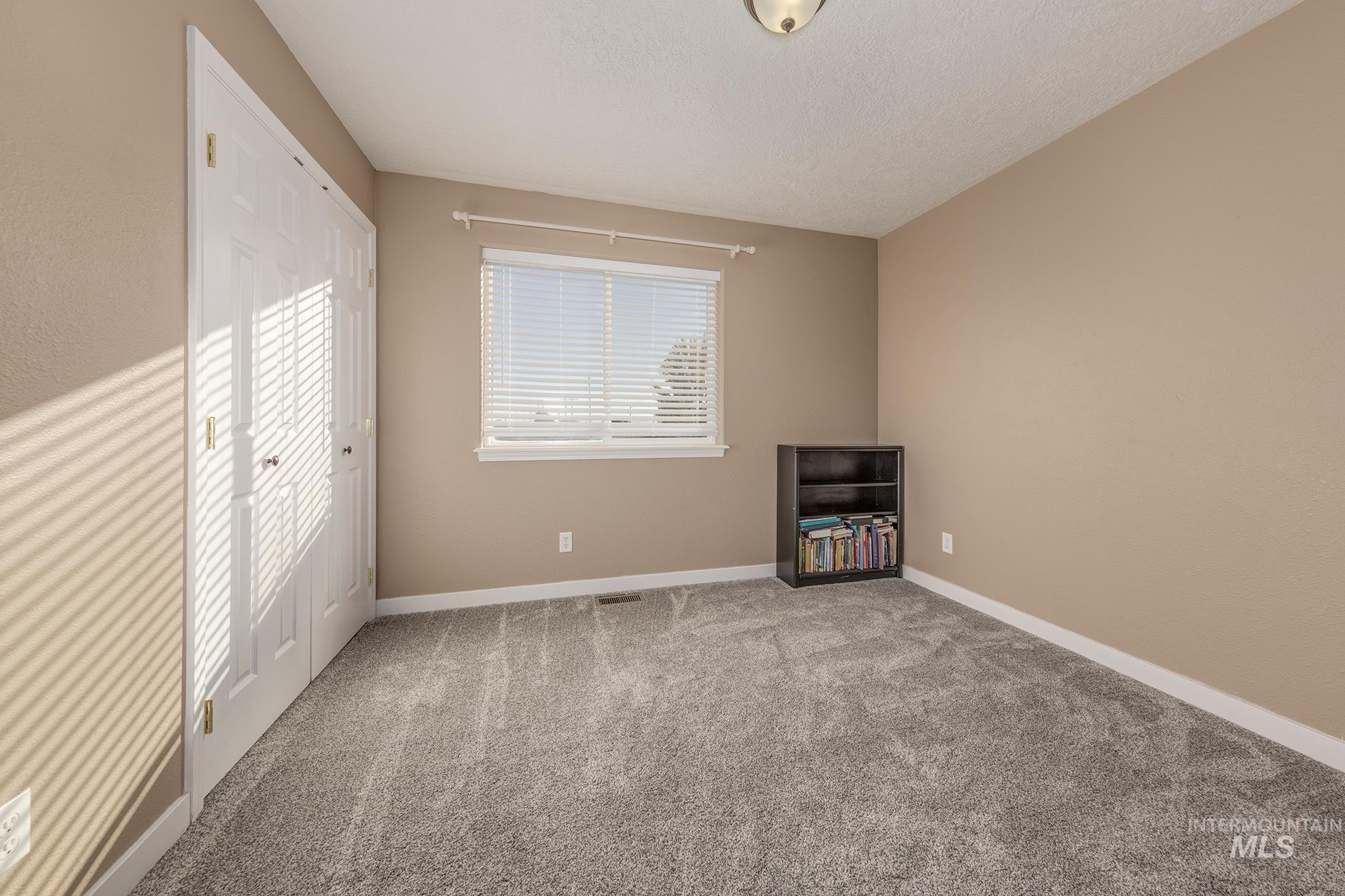 Unfurnished bedroom featuring a closet, multiple windows, light colored carpet, and a textured ceiling