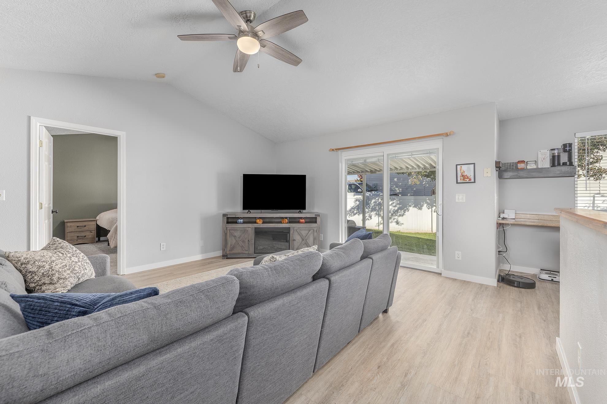 Living room featuring light wood-style floors, lofted ceiling, a ceiling fan, and a textured ceiling