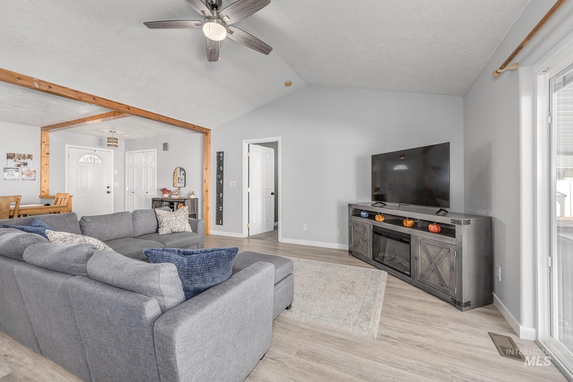 Living area featuring a textured ceiling, light wood-style flooring, ceiling fan, and vaulted ceiling