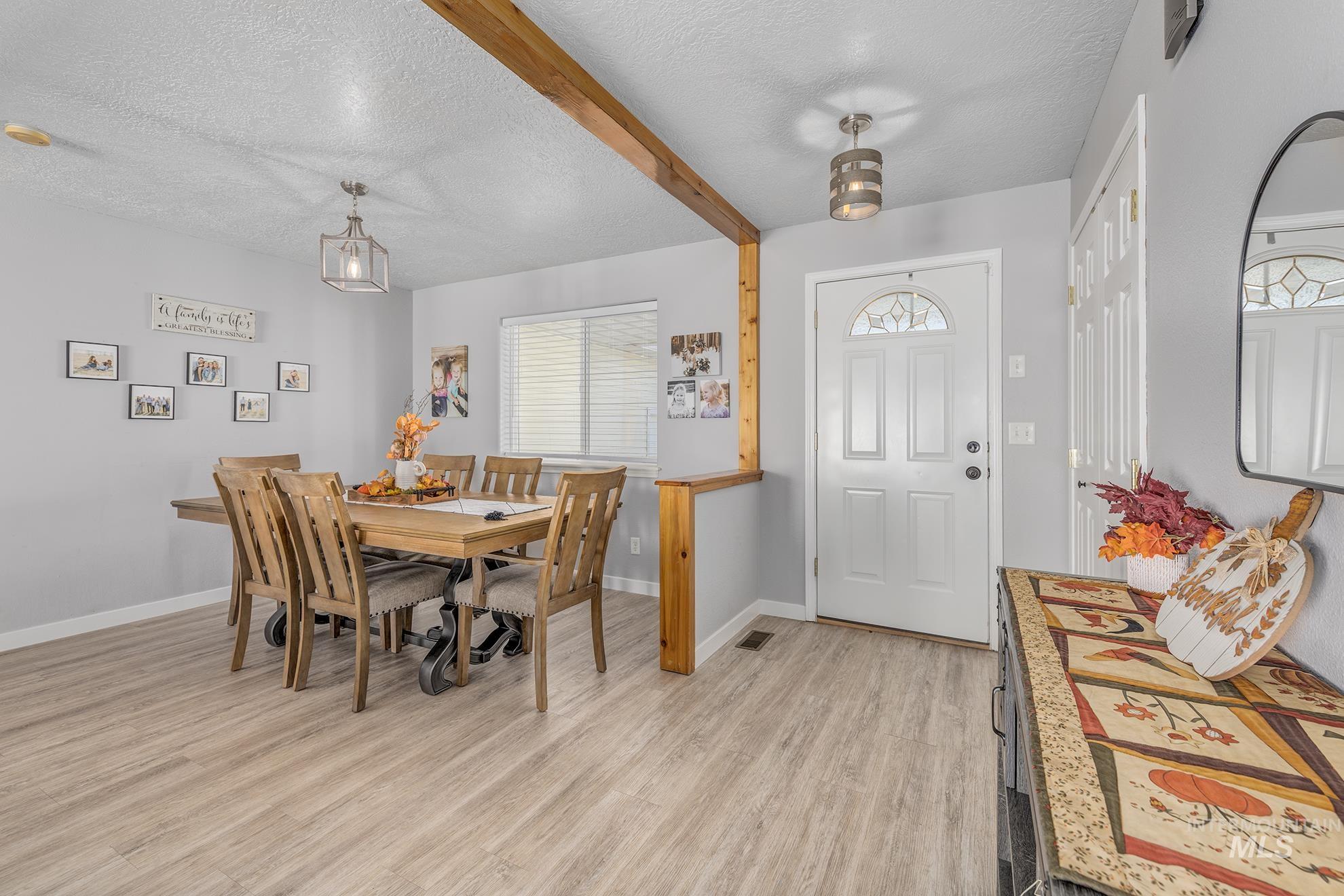 Dining room with a textured ceiling, light wood-style floors, and beamed ceiling
