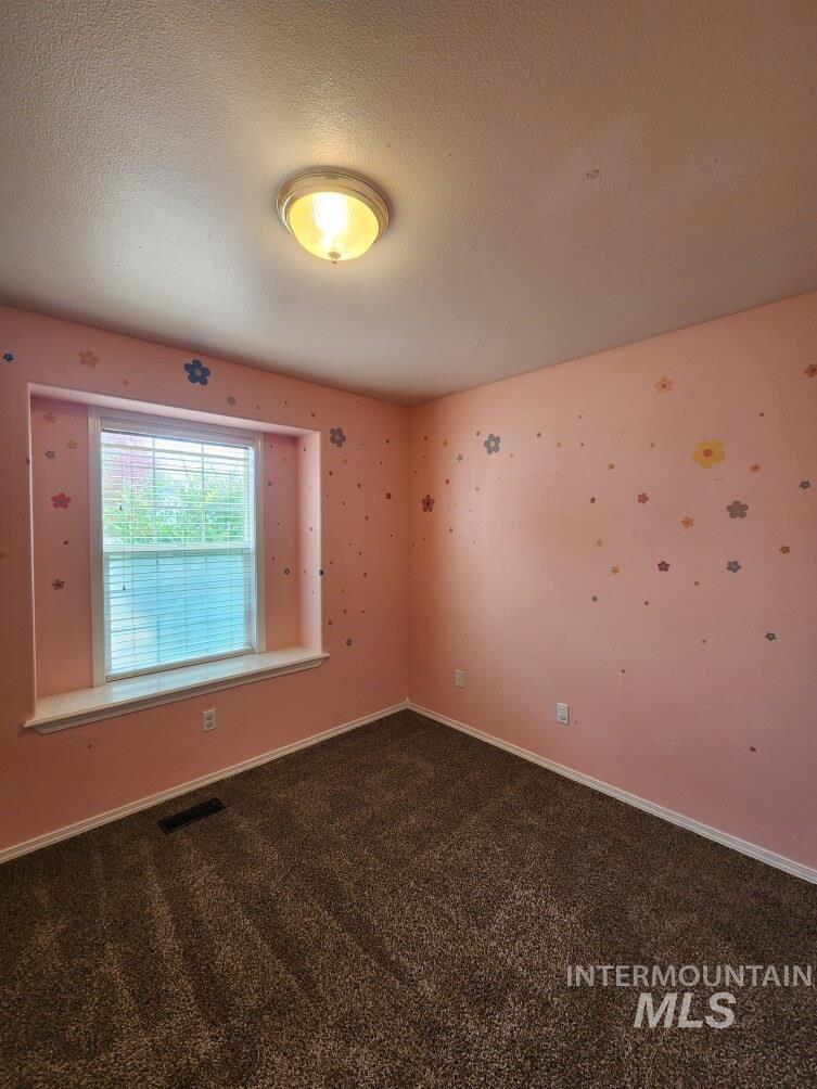 Empty room featuring dark colored carpet and a textured ceiling