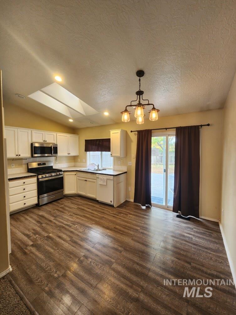 Kitchen with stainless steel appliances, white cabinets, dark wood-type flooring, a textured ceiling, and decorative light fixtures
