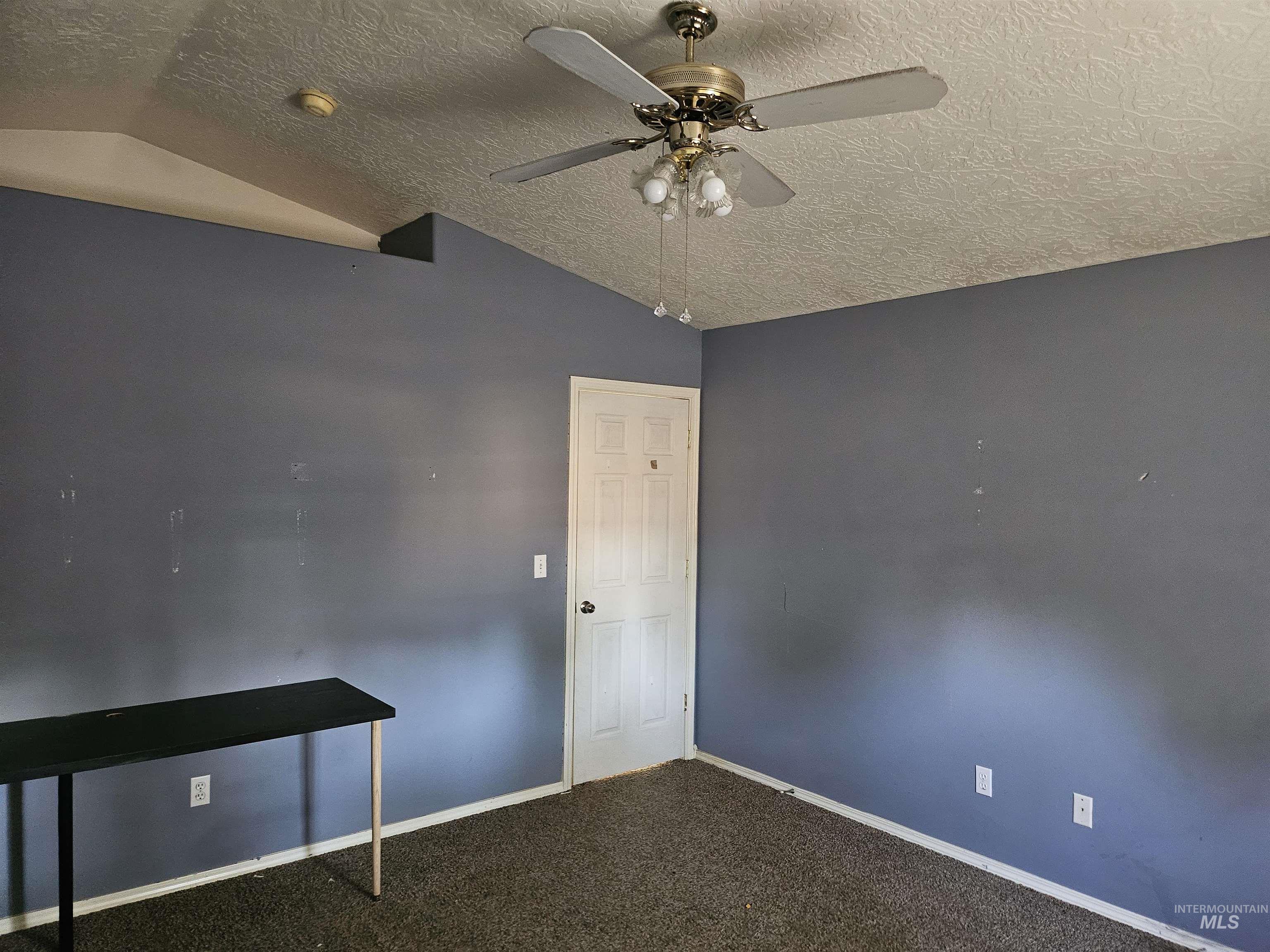 Empty room with vaulted ceiling, a textured ceiling, carpet flooring, and ceiling fan