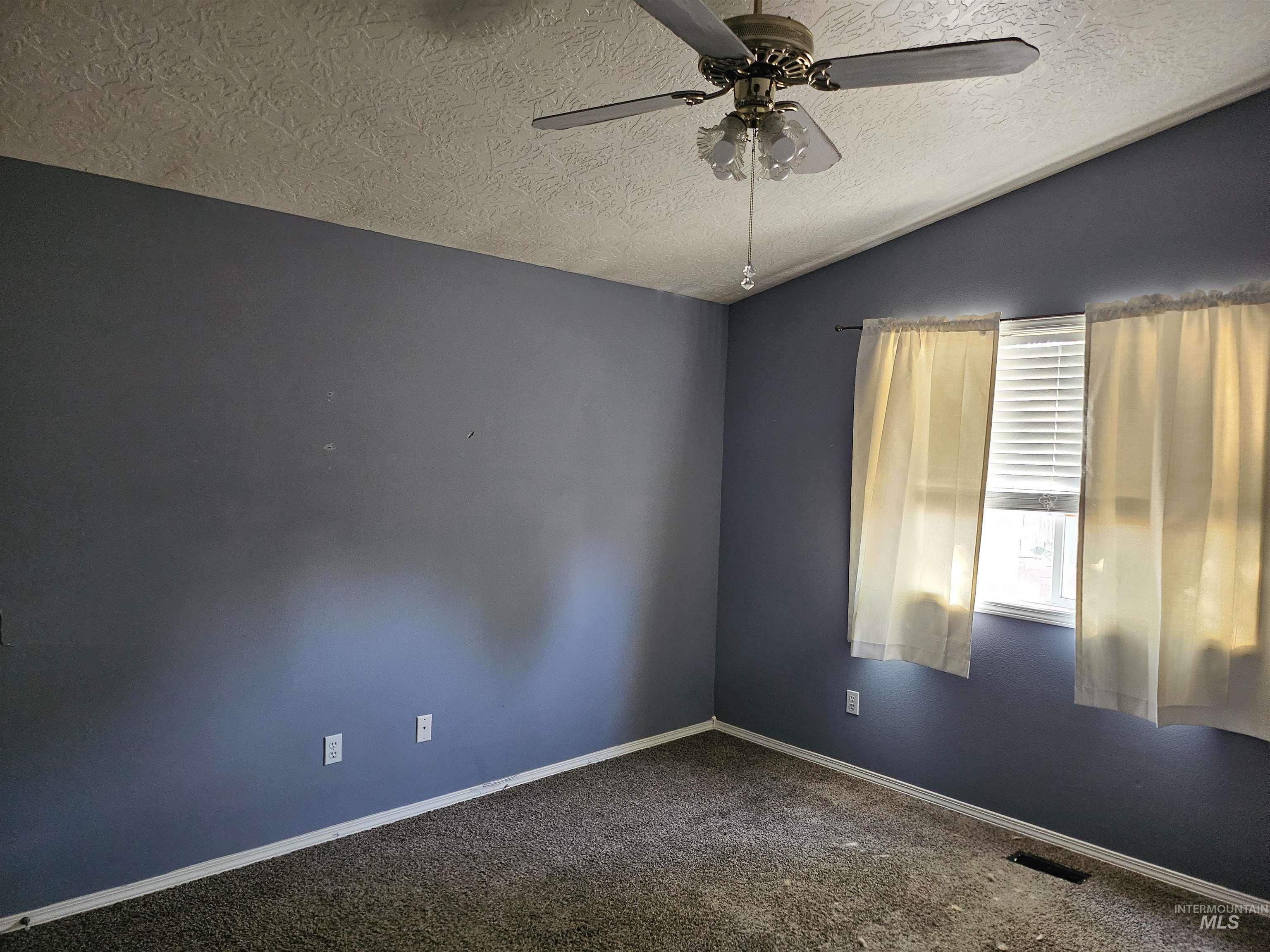 Unfurnished room featuring a textured ceiling, lofted ceiling, dark carpet, and a ceiling fan