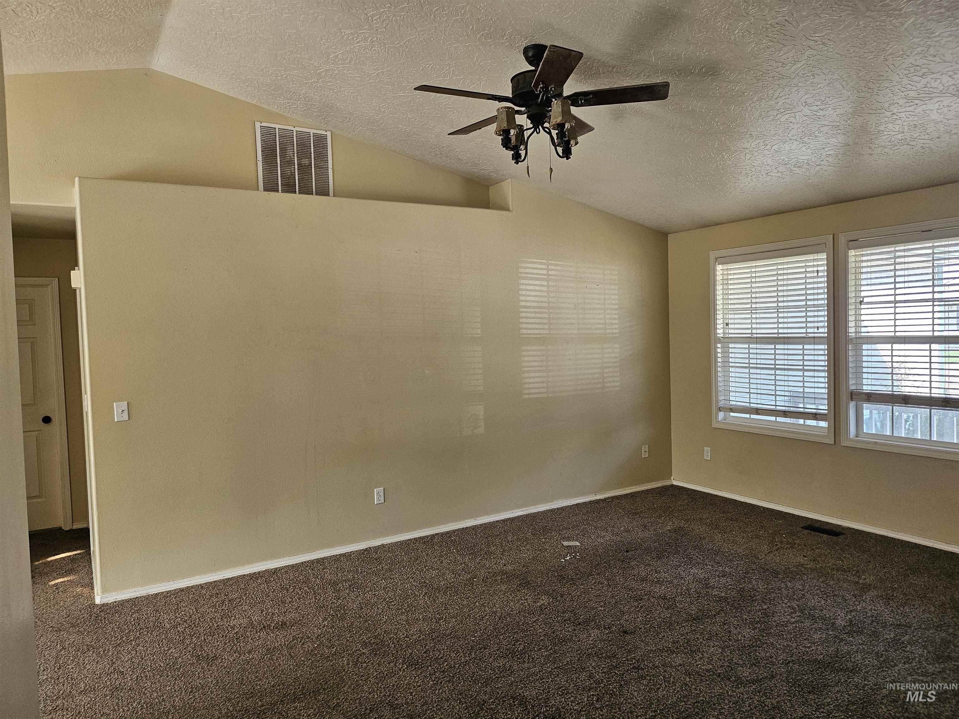 Spare room with a textured ceiling, dark carpet, vaulted ceiling, and a ceiling fan