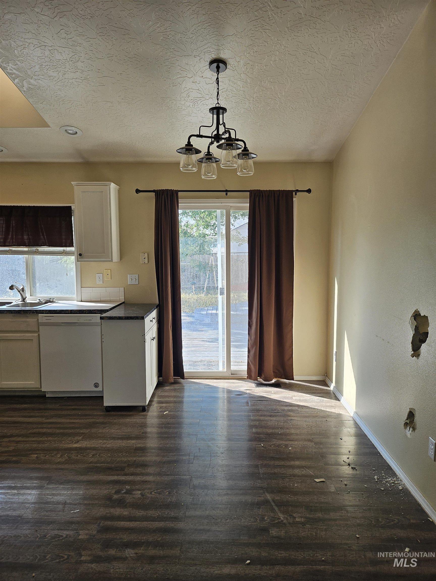 Kitchen featuring white cabinets, white dishwasher, dark wood-type flooring, decorative light fixtures, and dark countertops