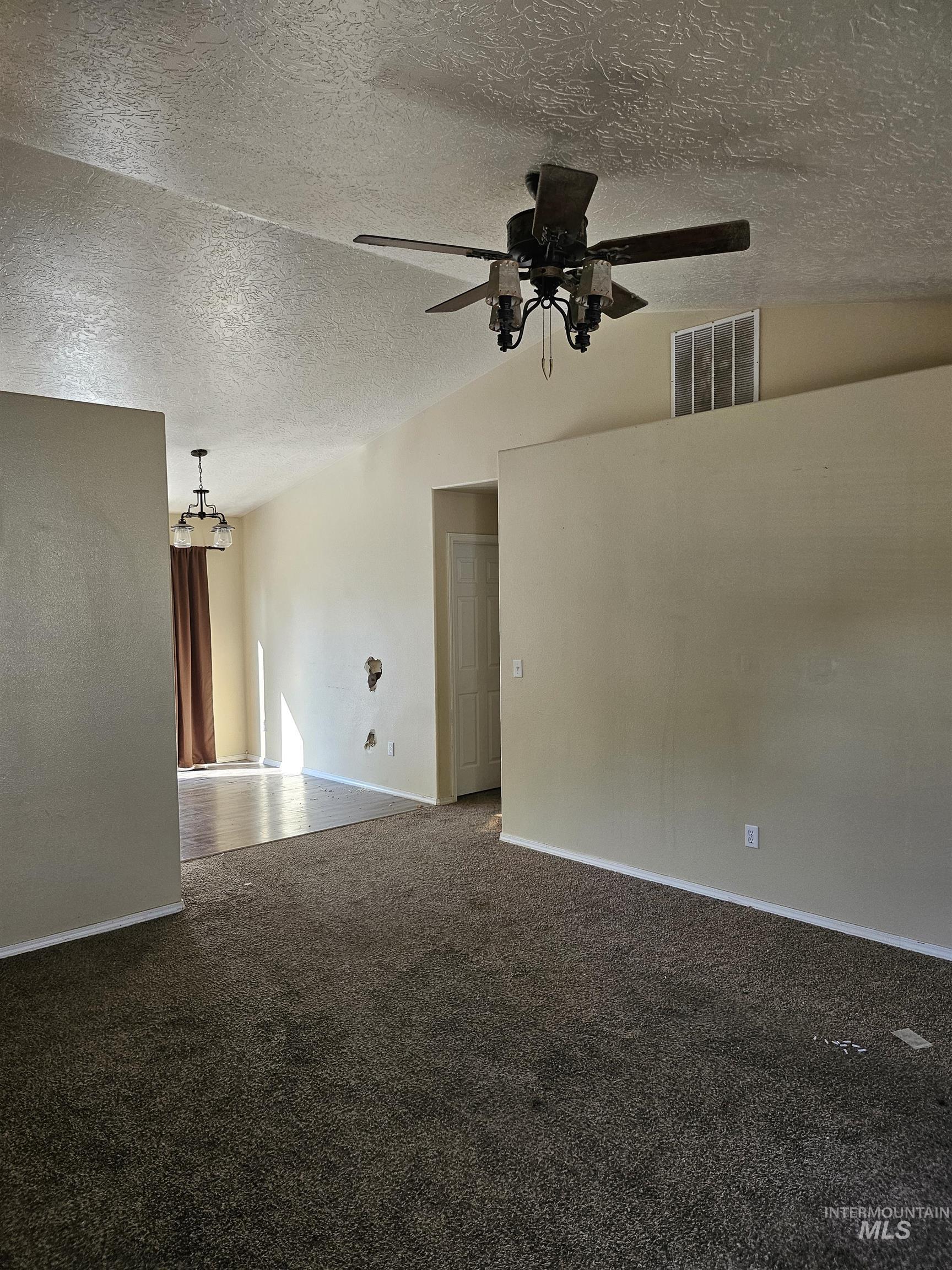 Empty room with lofted ceiling, a textured ceiling, dark carpet, and ceiling fan