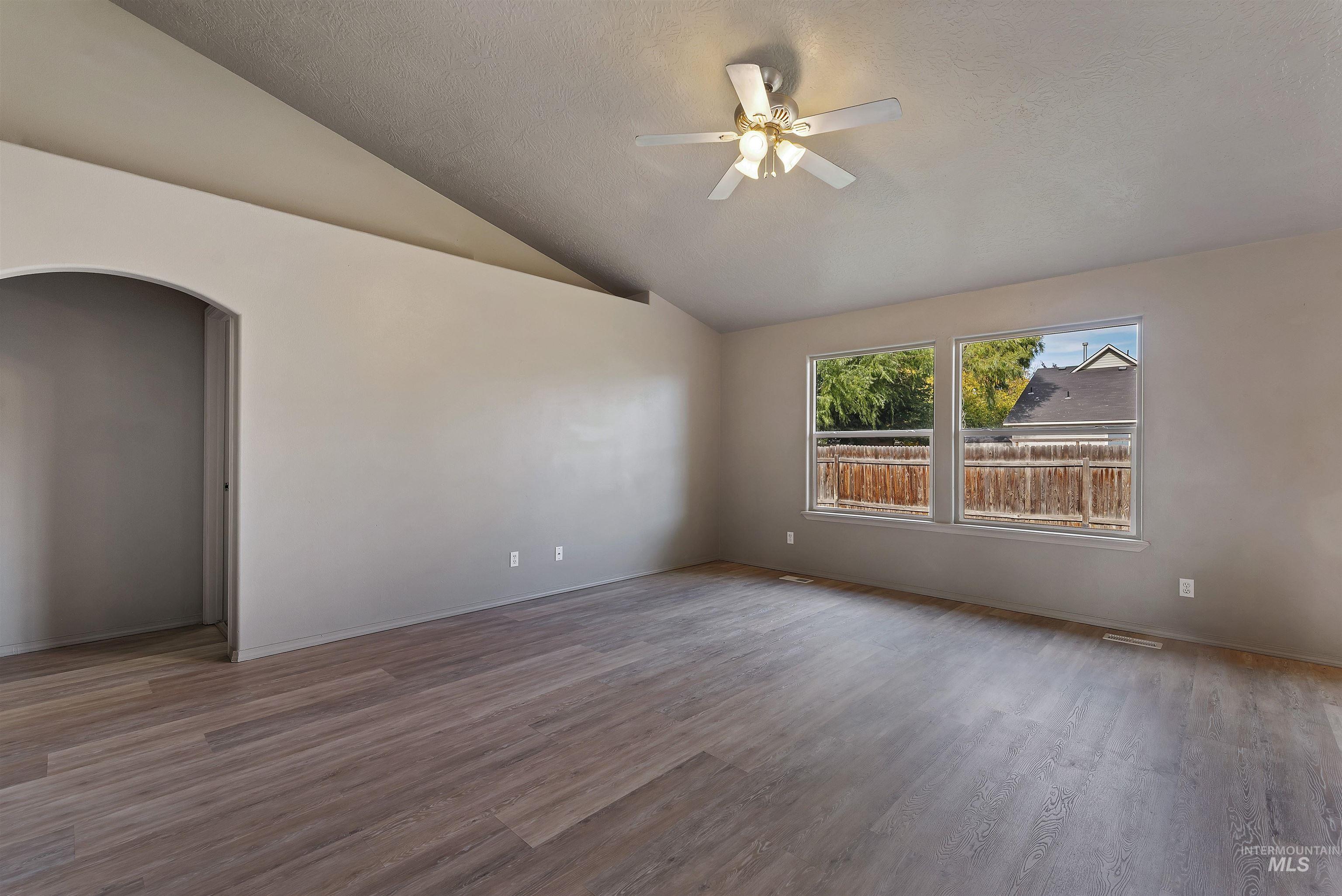 Spare room with wood finished floors, lofted ceiling, arched walkways, a textured ceiling, and a ceiling fan