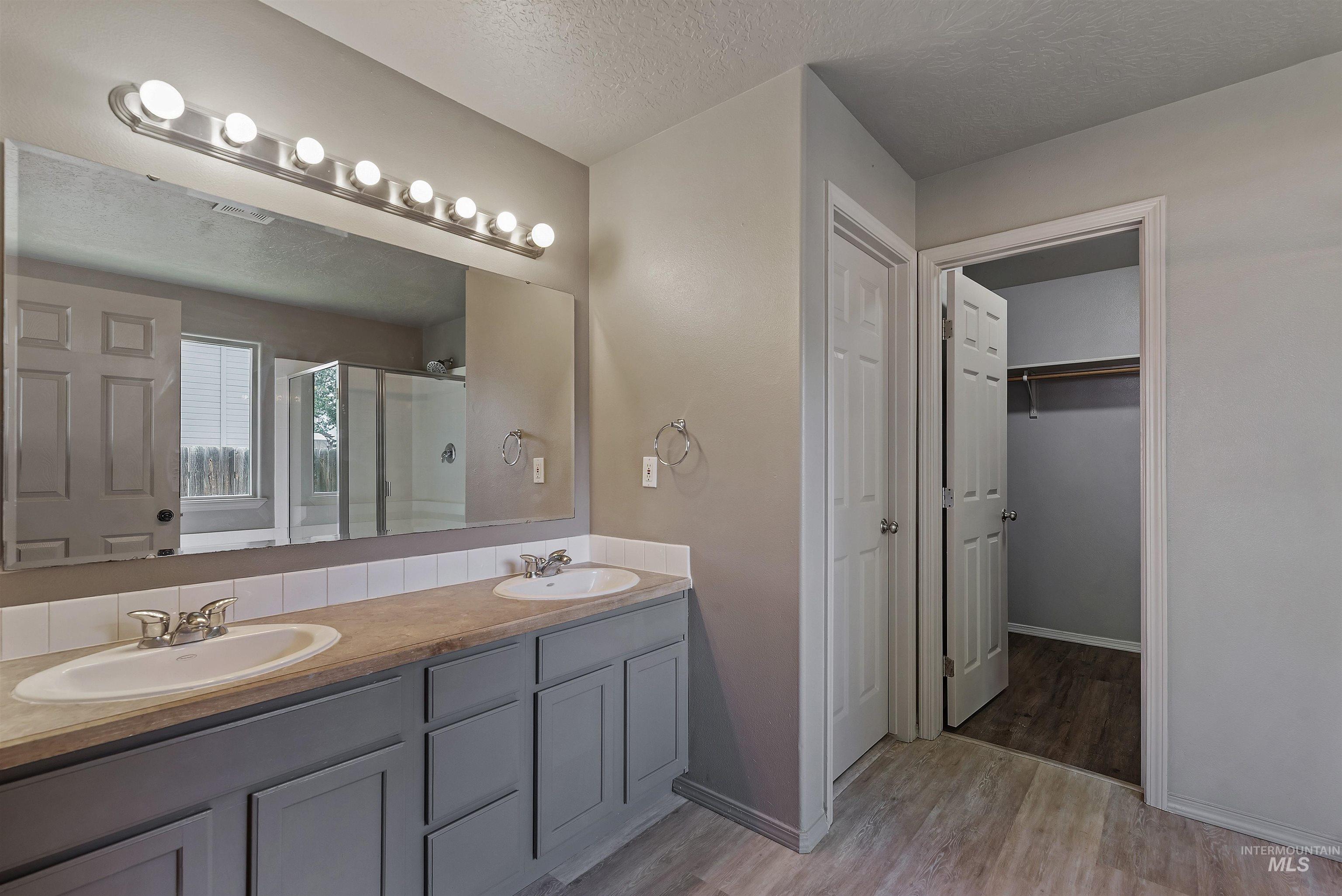 Bathroom with a textured ceiling, light wood-style floors, a shower stall, double vanity, and a spacious closet