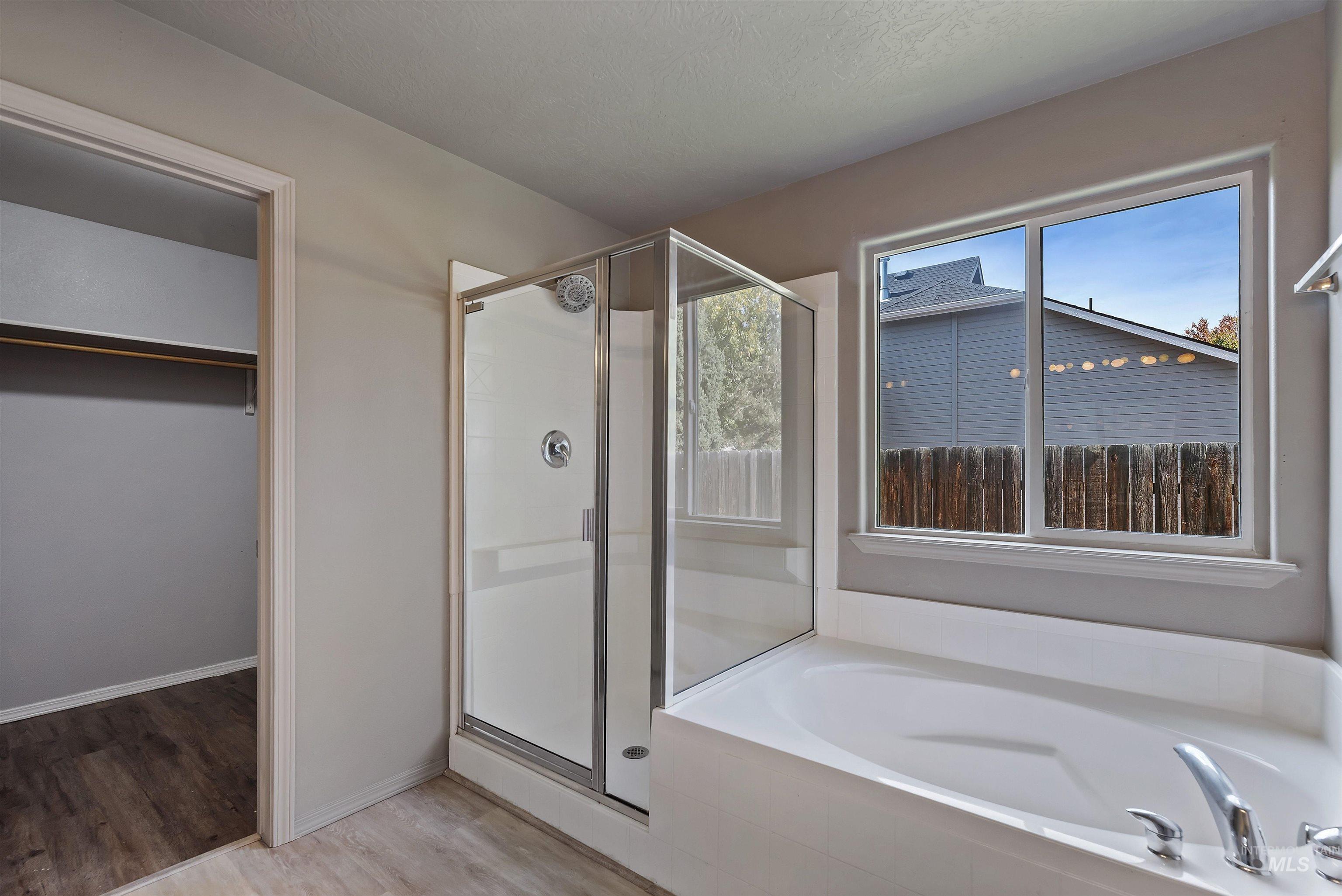Full bath with light wood-type flooring, a walk in closet, a stall shower, and a bath