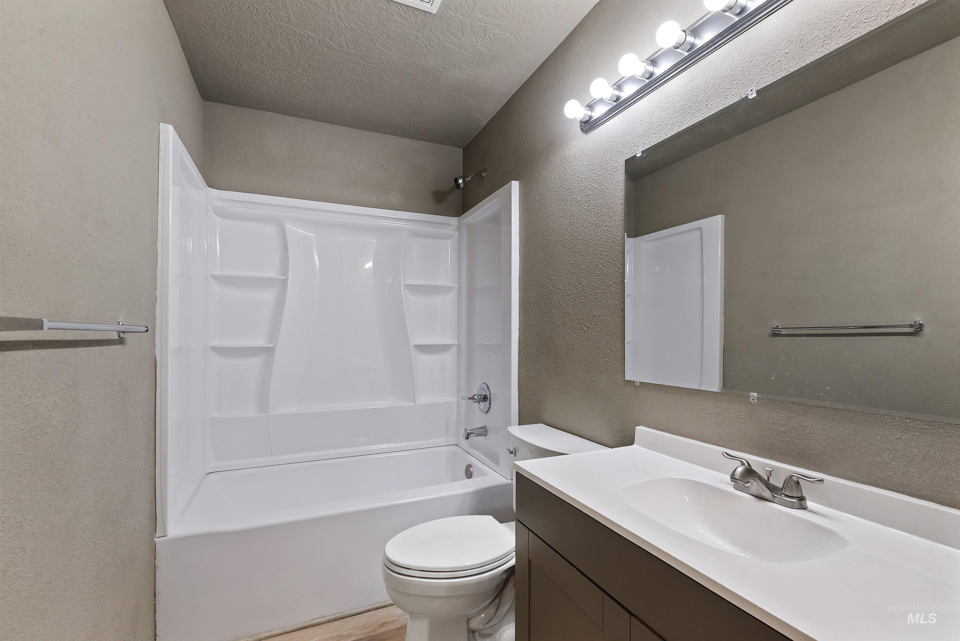 Full bathroom with a textured wall, shower / tub combination, a textured ceiling, and vanity