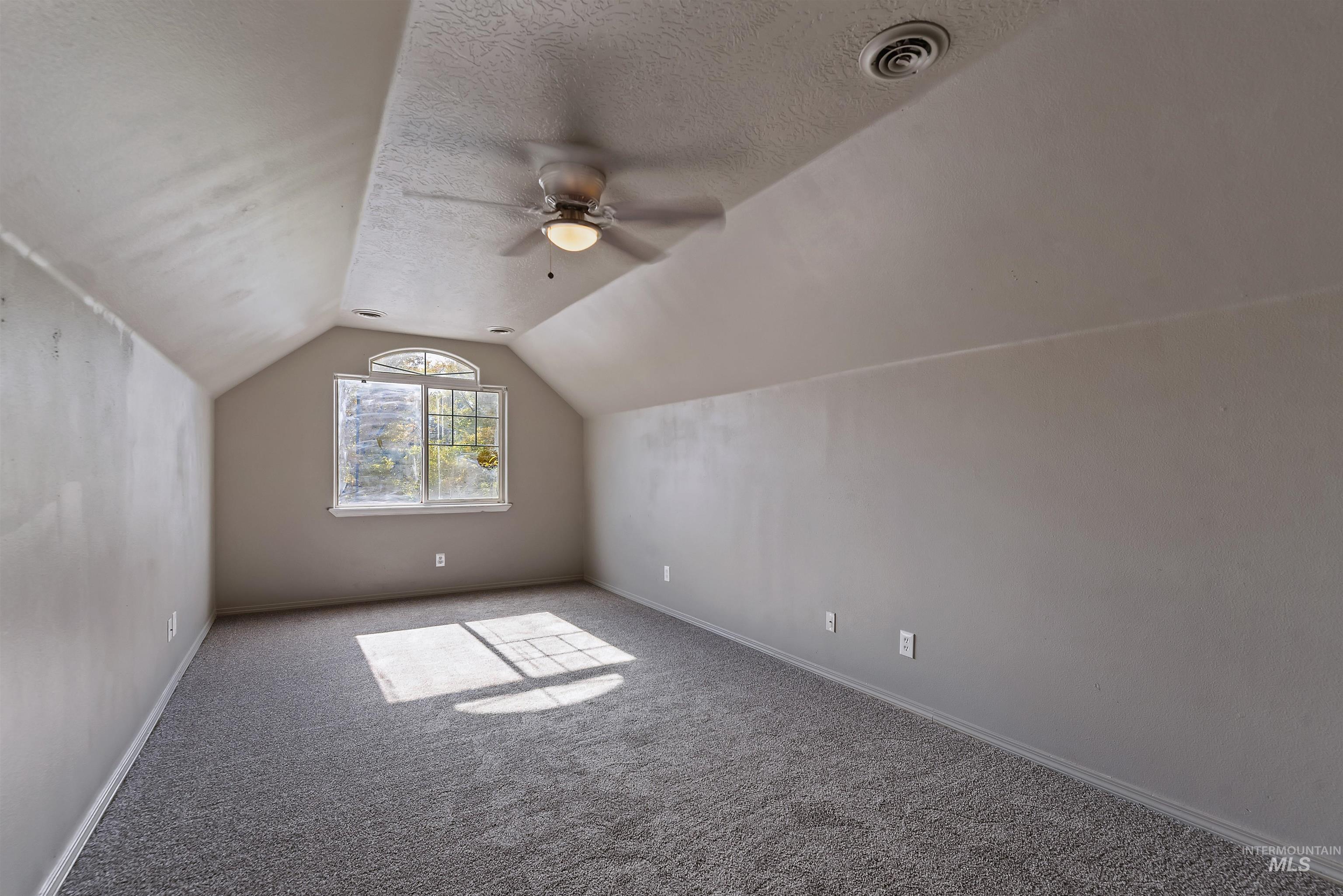 Additional living space with carpet, a textured ceiling, vaulted ceiling, and ceiling fan