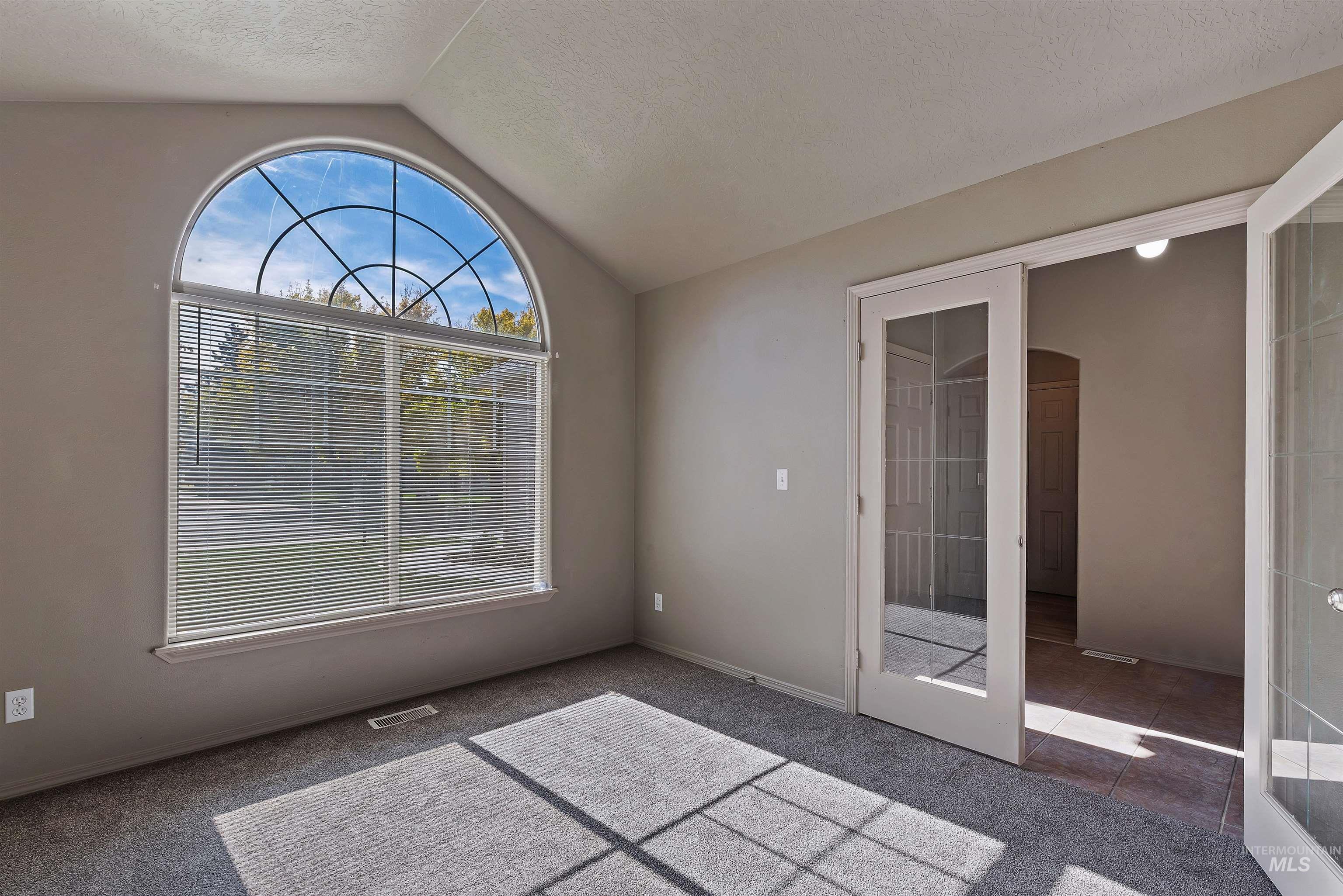 Carpeted empty room with vaulted ceiling, french doors, tile patterned flooring, and a textured ceiling